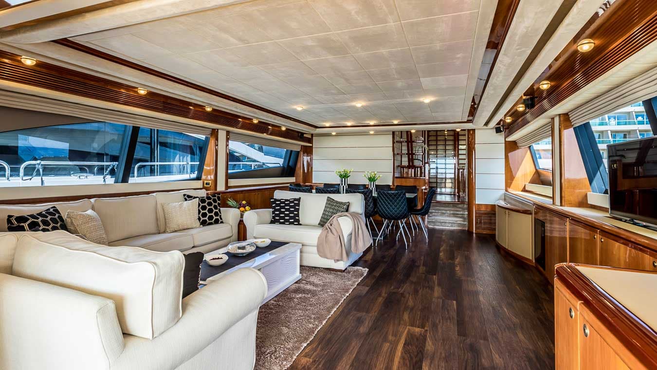 Luxury yacht salon with white sofas, dark wood floors, and dining area visible through windows.