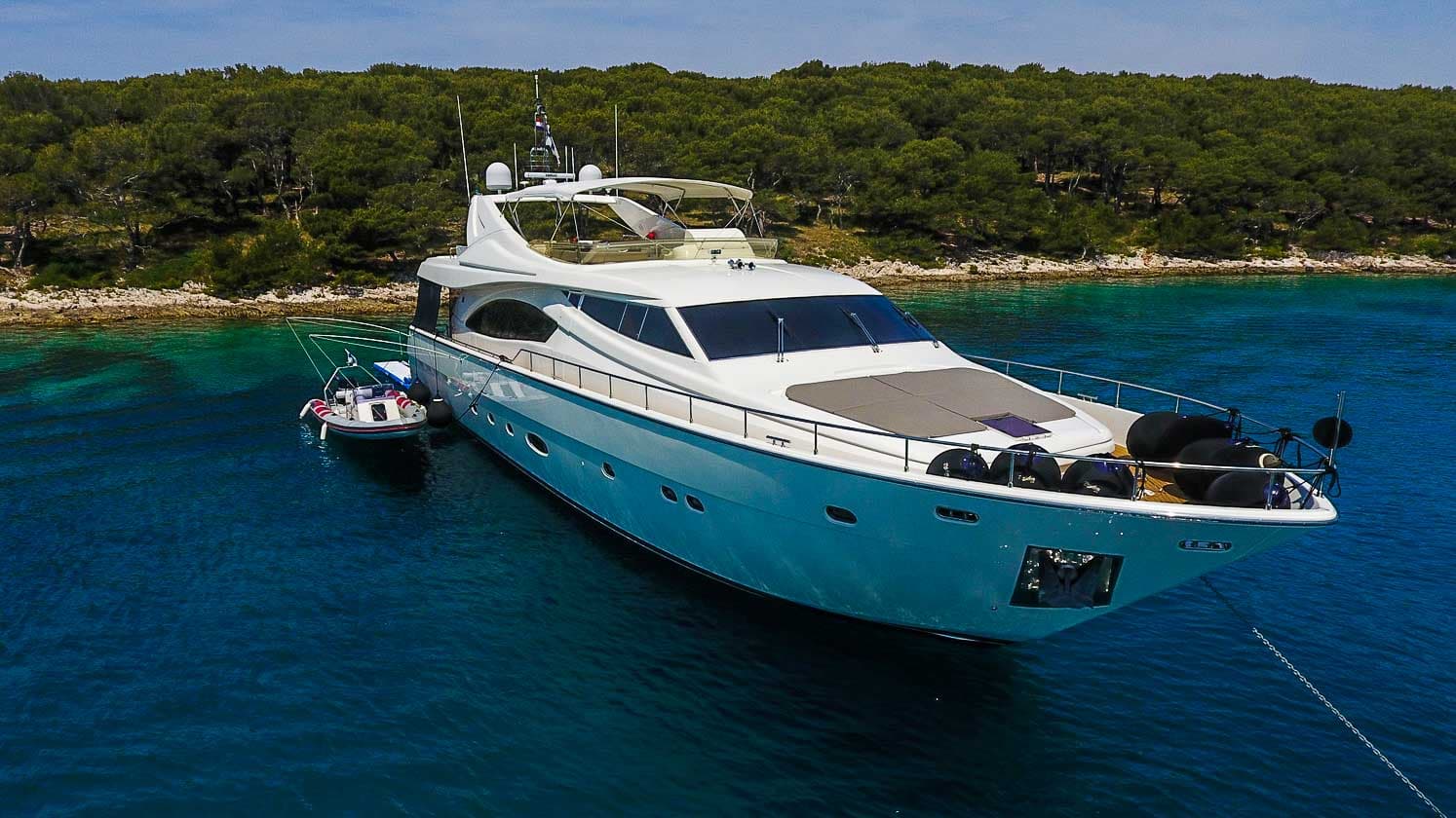 Luxury motor yacht anchored near a wooded coastline in clear blue water