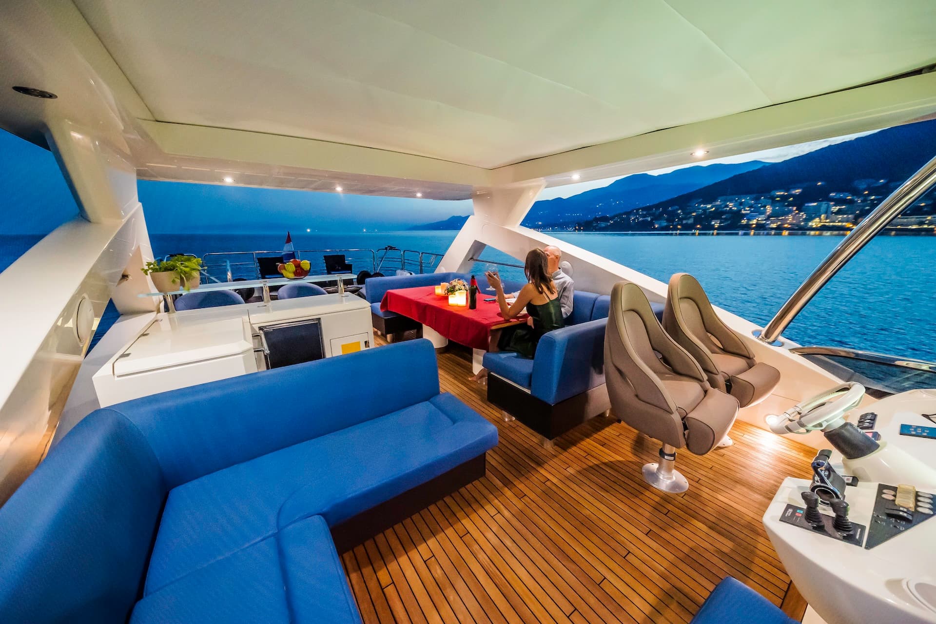Yacht deck dining at dusk with couple overlooking illuminated coastline and mountains in Croatia.