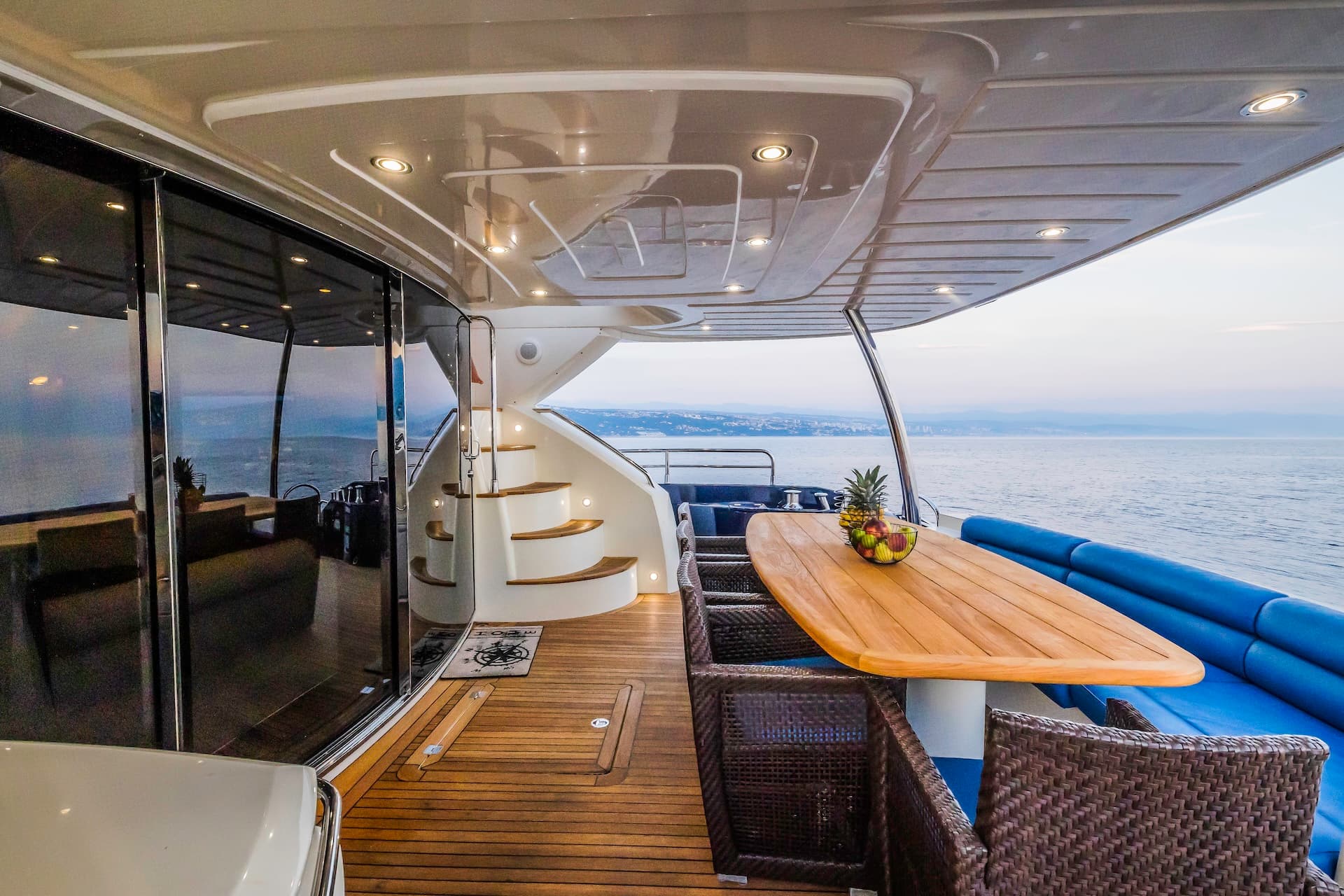 Aft deck of a yacht with teak flooring, dining table, and view of the Croatian coastline.