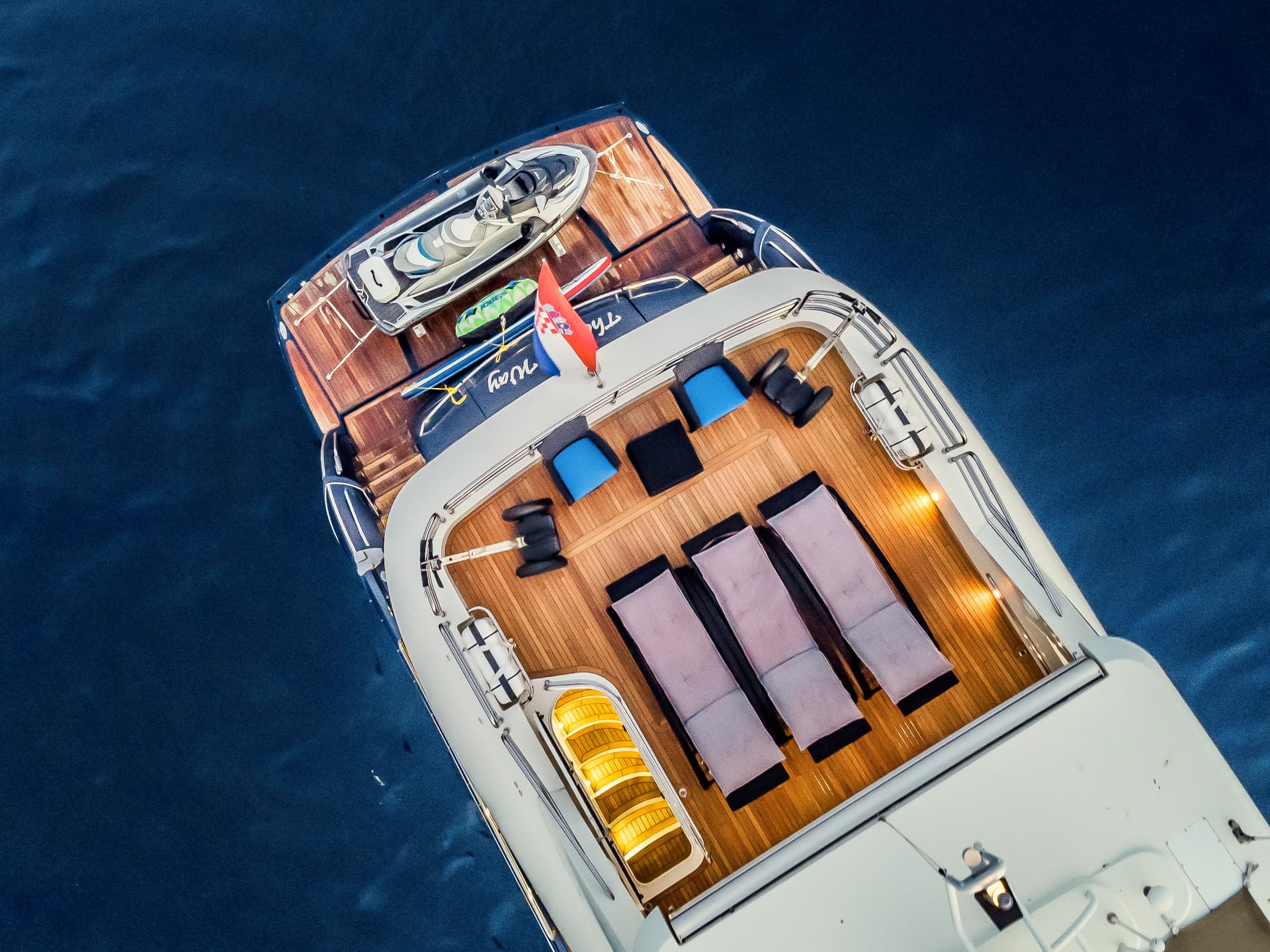 Luxury yacht stern with teak deck, sun loungers, and jet ski on deep blue water.