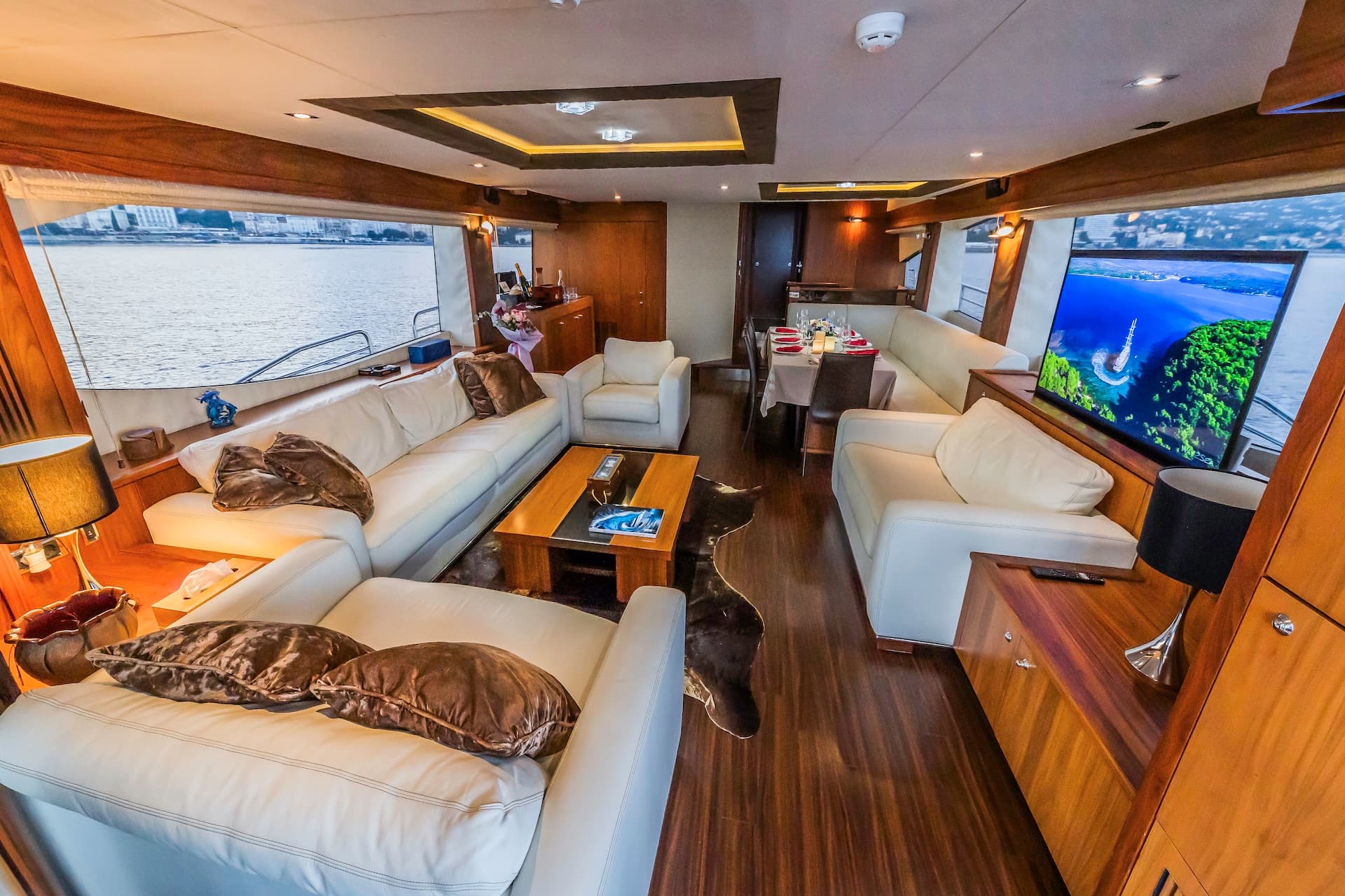 Luxury yacht interior with white leather seating, wood floors, and view of coastal city.