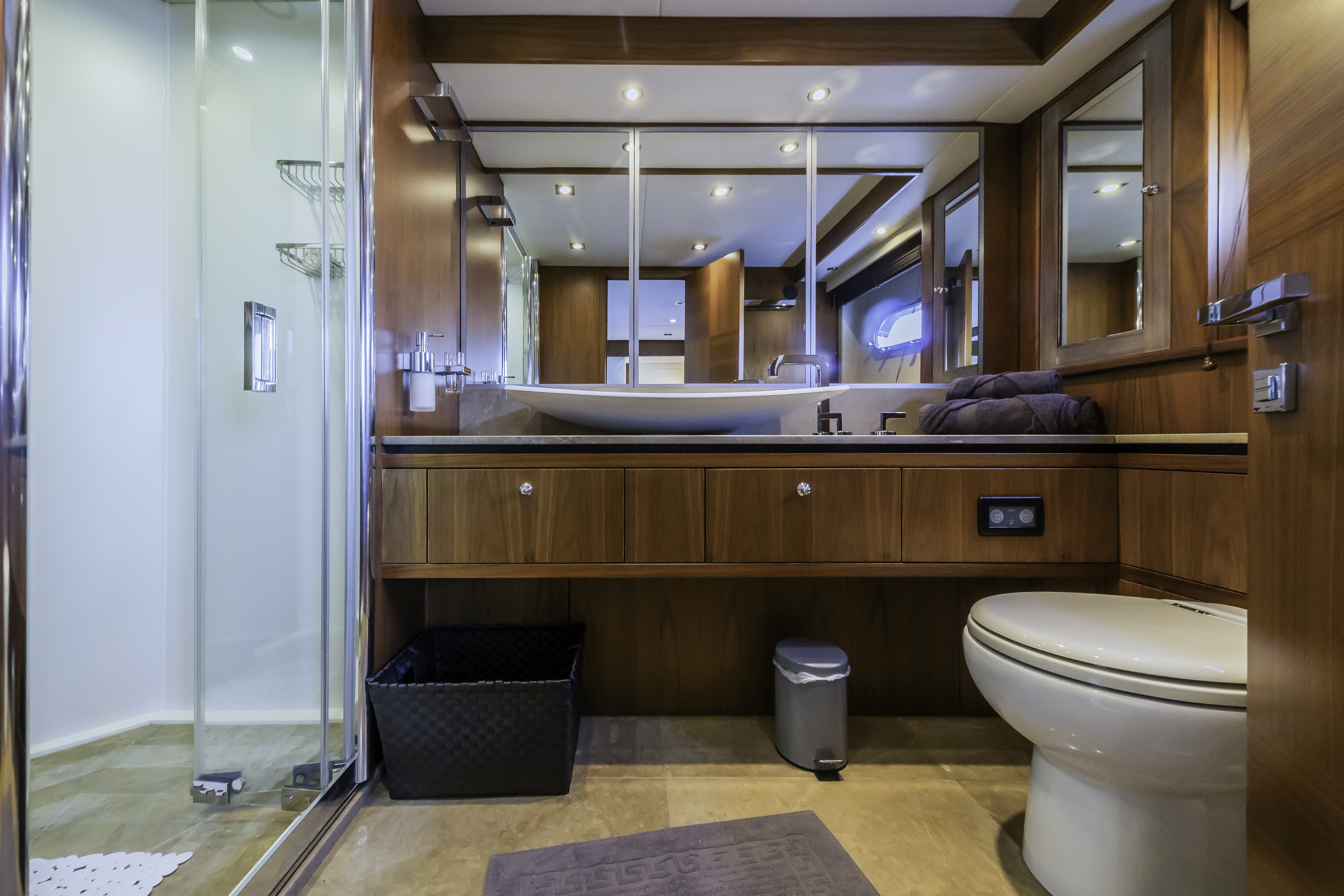 Yacht bathroom interior with wood paneling, vessel sink, glass shower, and toilet.