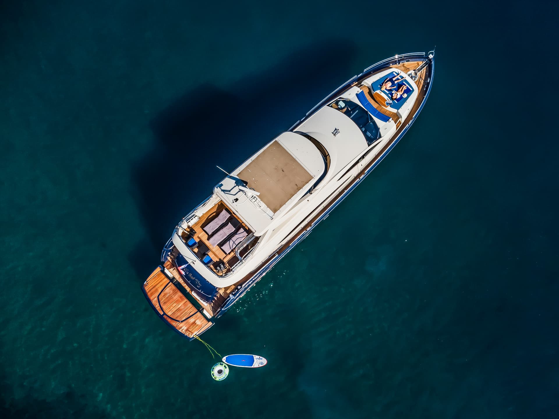 Aerial view of luxury yacht anchored on deep blue water with paddleboard and towable tube.