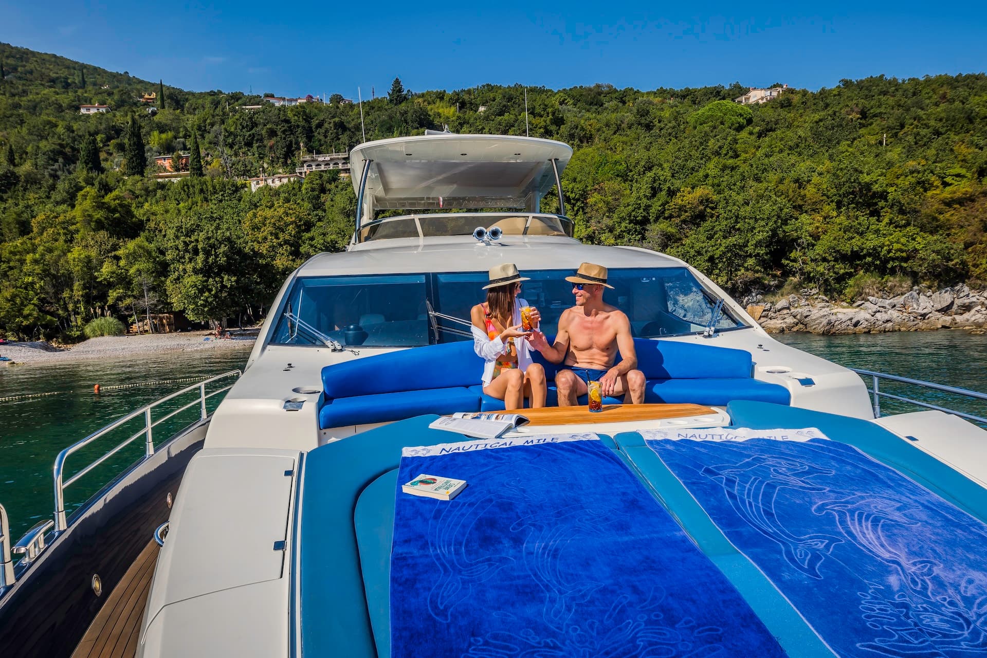 Couple relaxing on yacht deck with drinks near lush green Croatian coastline