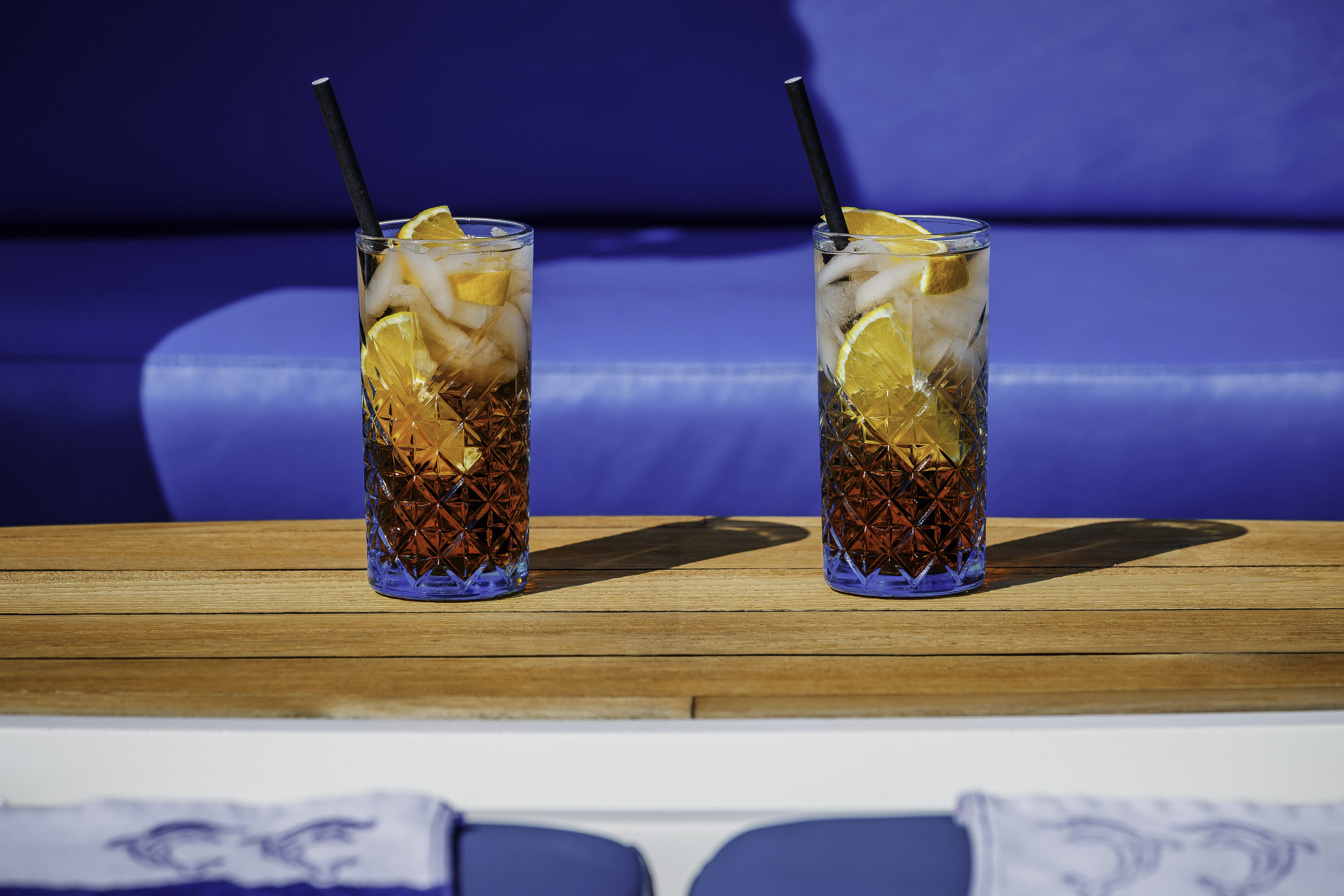 Two cocktails with orange slices and ice on a wooden deck with blue background, likely on a yacht in Croatia.