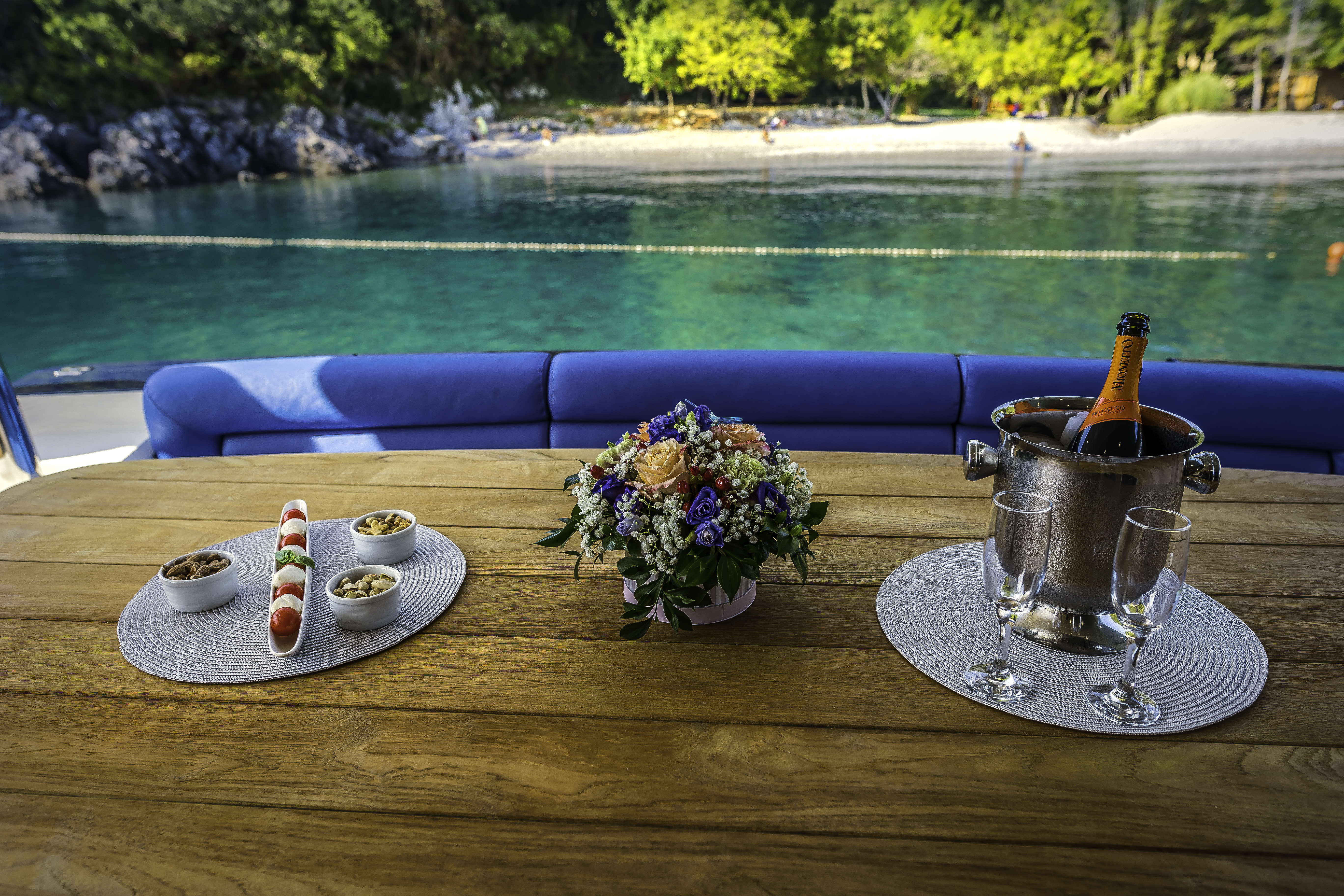 Yacht table setting with Prosecco, snacks, and flowers overlooking turquoise Croatian cove.