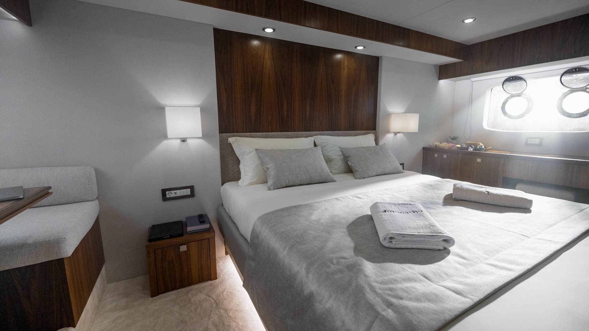 Master cabin bedroom with double bed, wood paneling, and porthole windows suggesting a boat setting.