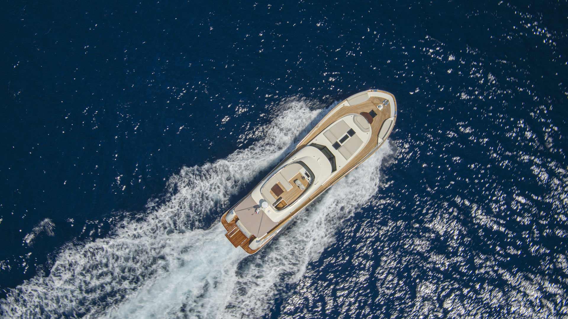 Motor yacht speeding across deep blue water leaving white wake, aerial view