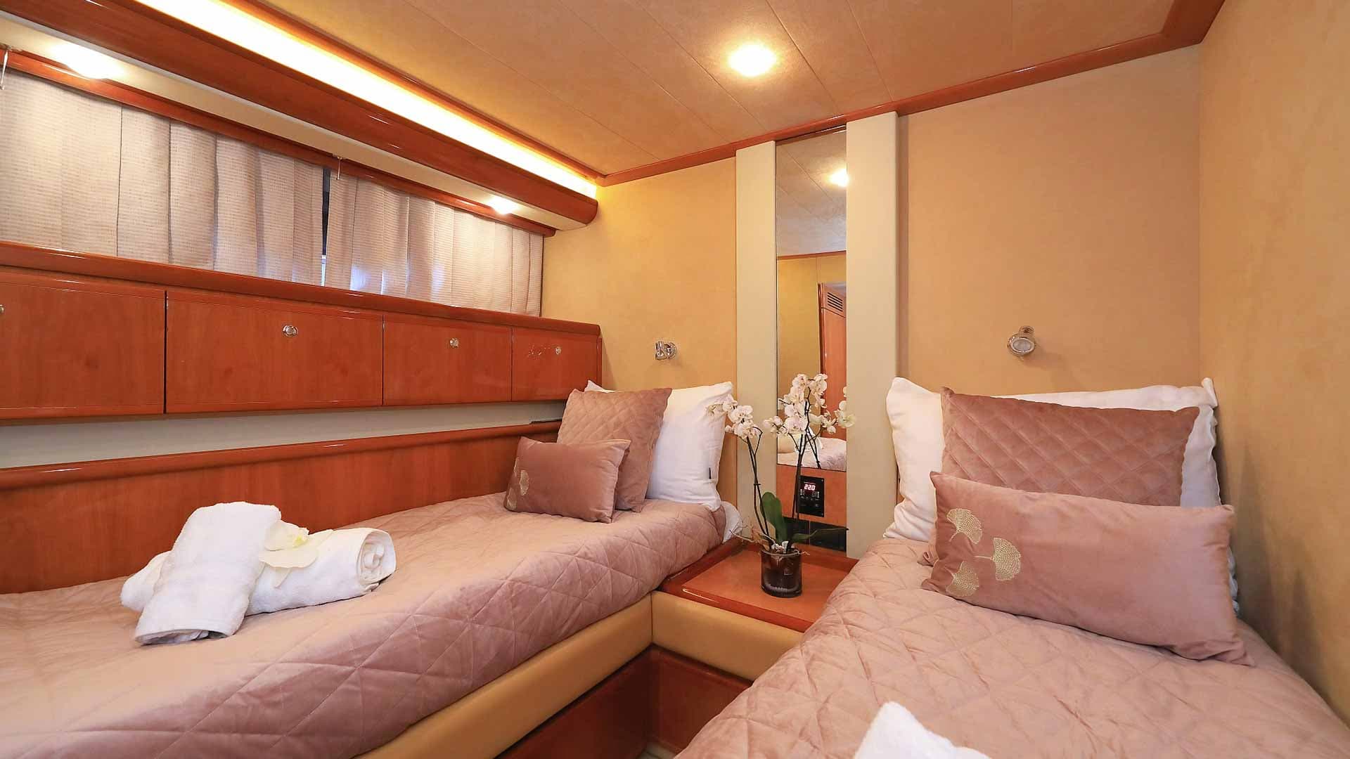 Twin cabin interior on a yacht with wood paneling, pink bedding, and white towels.