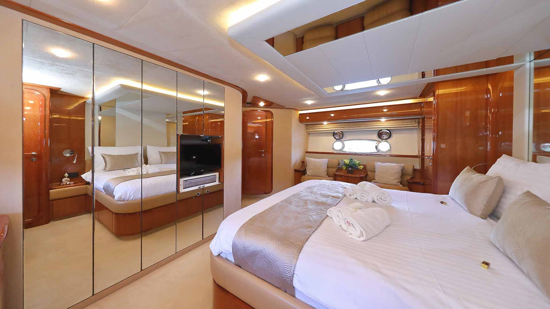 Yacht cabin bedroom with white bedding, mirrored closets, and porthole windows.