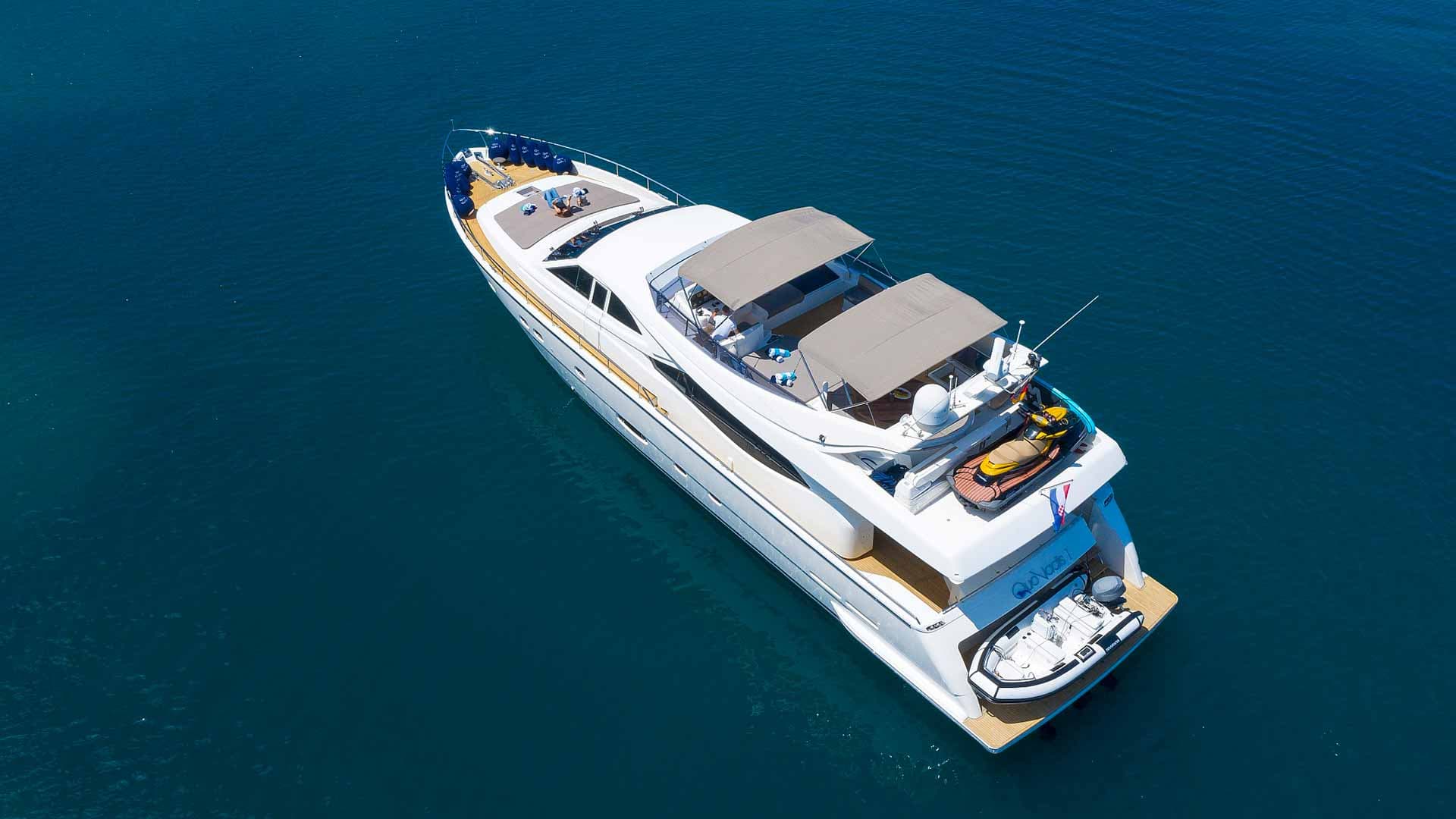 White motor yacht named Quo Vadis with jet ski and dinghy anchored in deep blue water.