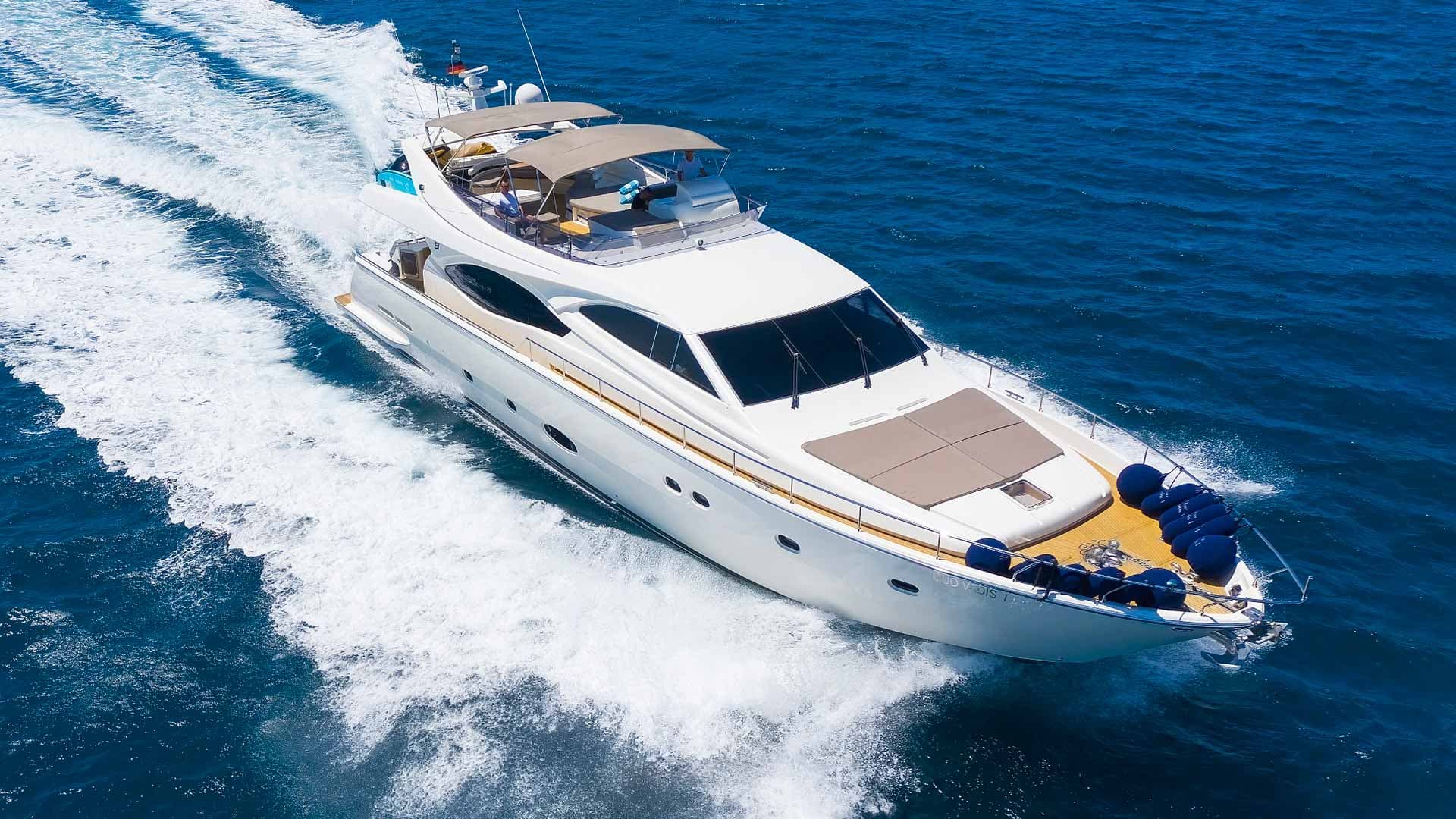 White motor yacht named "Quo Vadis" speeding across deep blue coastal waters.