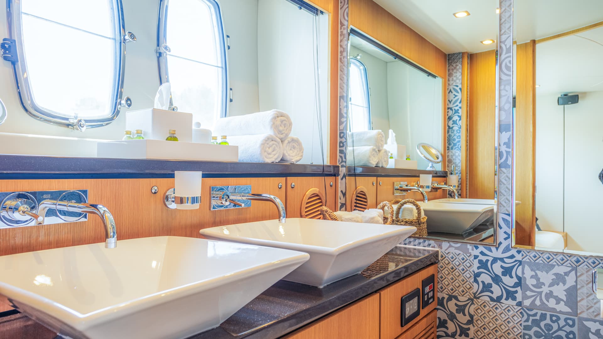 Master cabin bathroom with dual vessel sinks, wood paneling, and oval porthole windows.