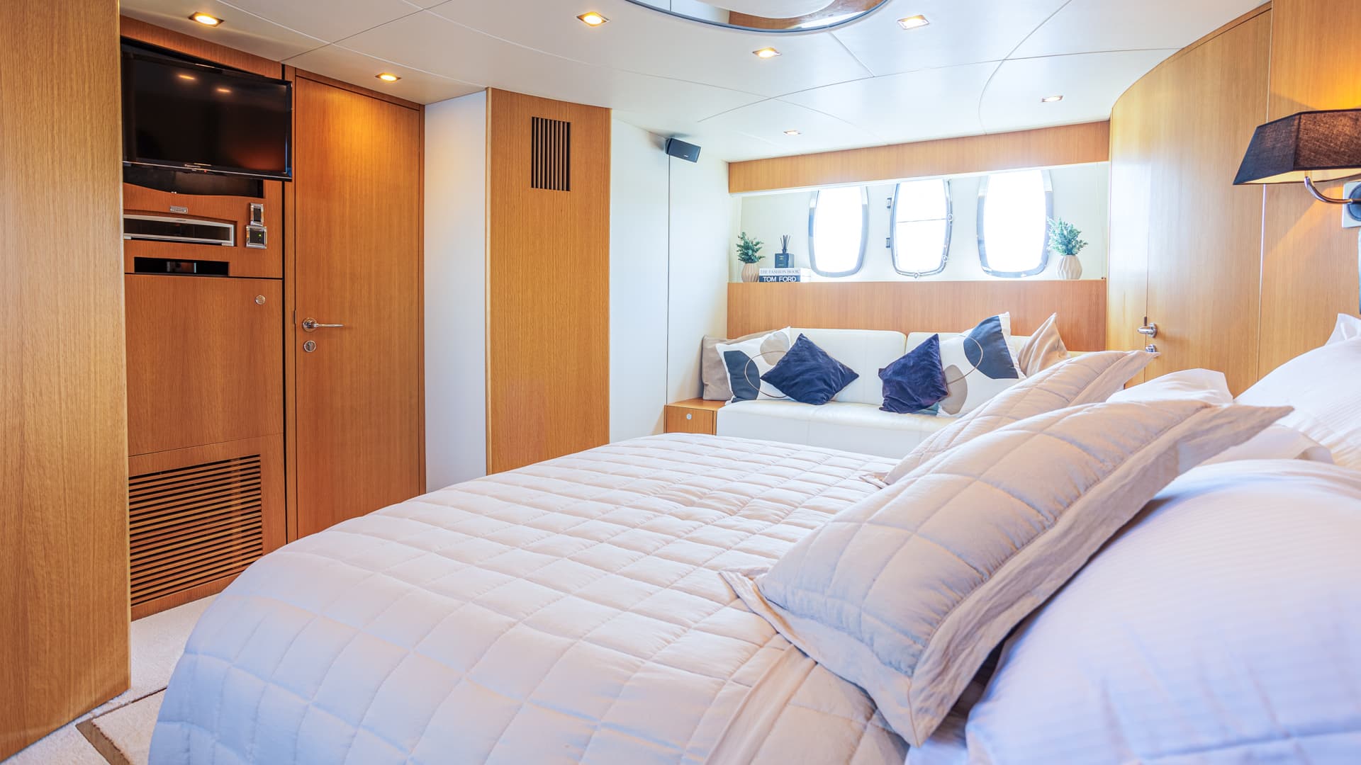 Master cabin interior with wood paneling, white bedding, and porthole windows on a yacht.