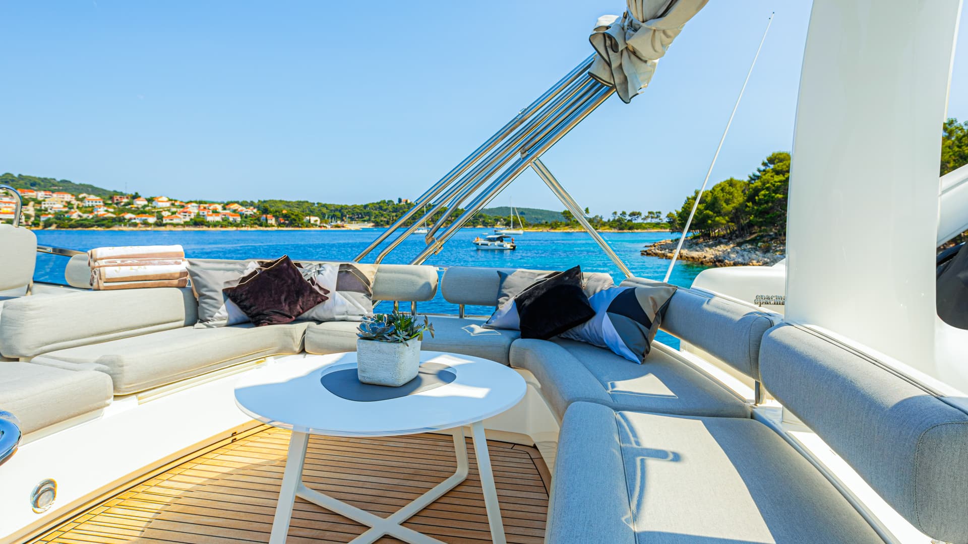 Flybridge seating area on yacht with cushions, white table, and coastal town view.