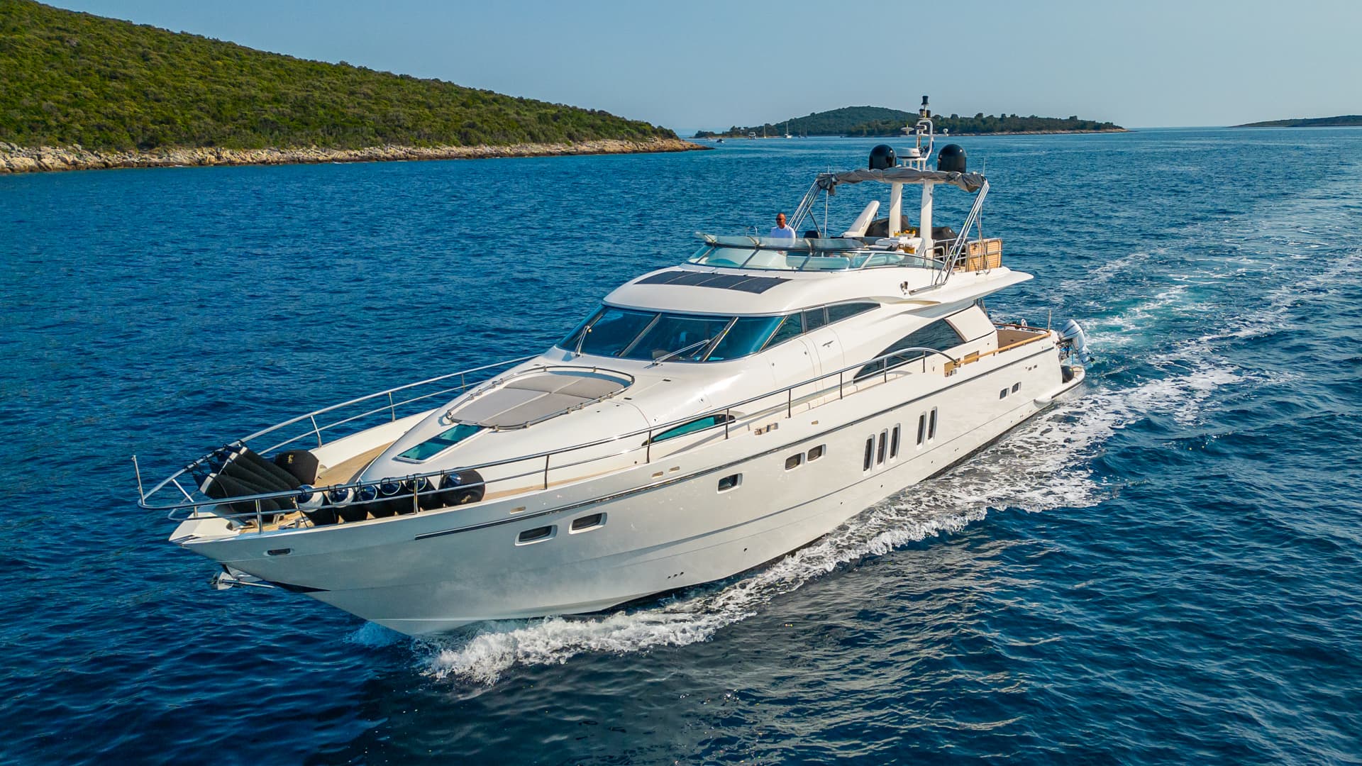 White motor yacht speeding through deep blue coastal waters near a green island