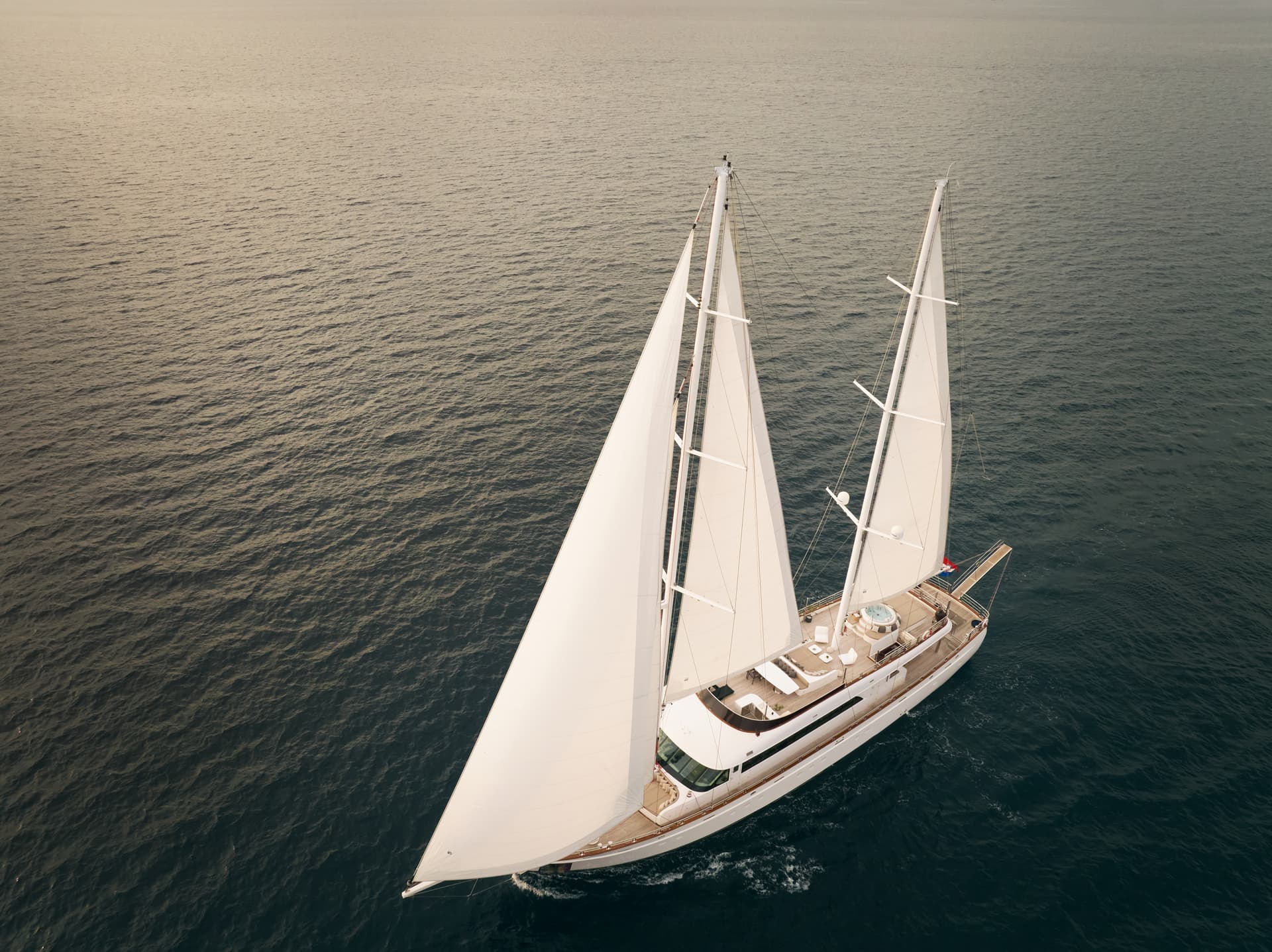 Large luxury sailing yacht with white sails cruising on dark, rippling sea water.