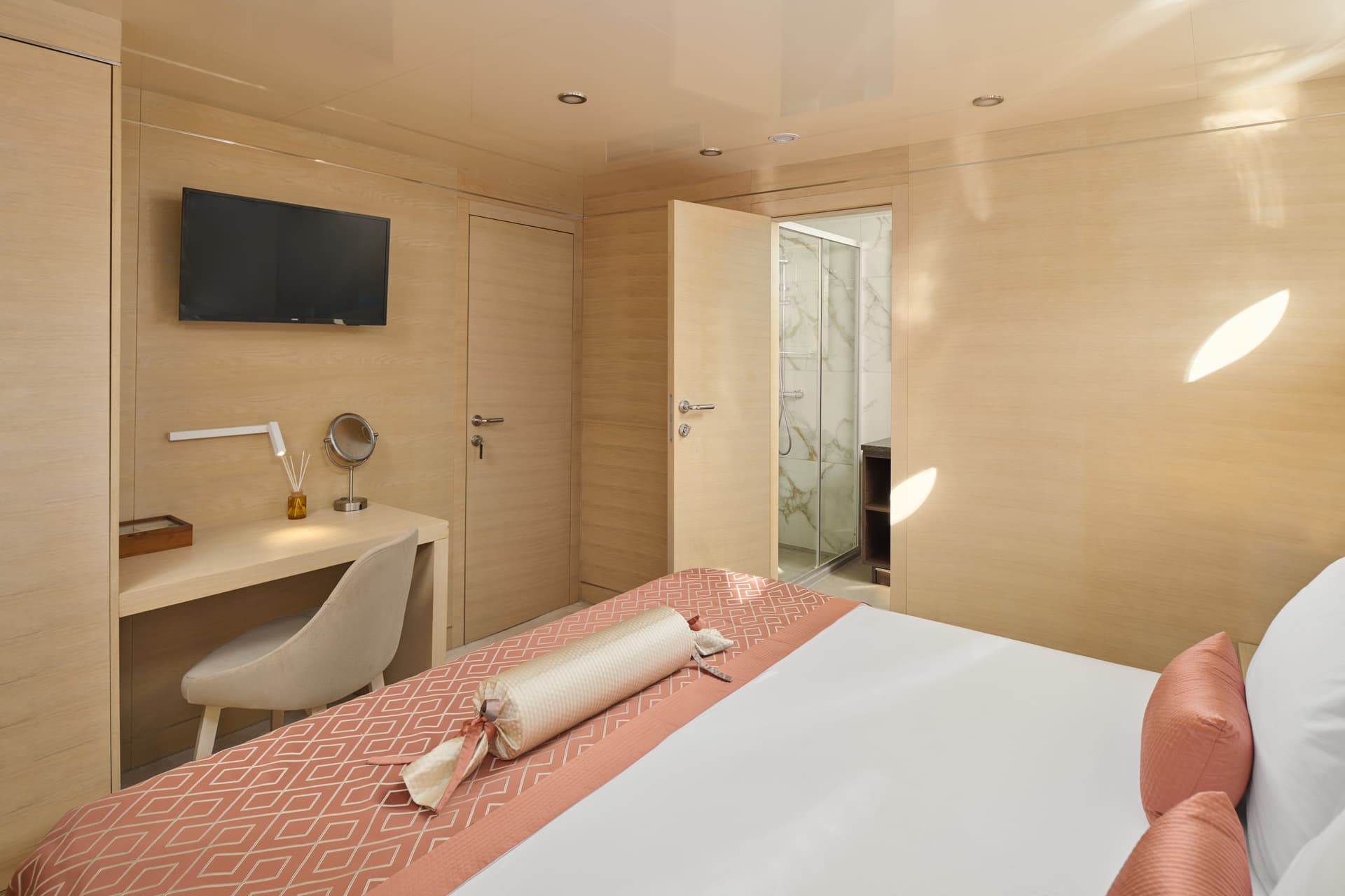 Modern yacht cabin bedroom with light wood paneling and view into marble bathroom.
