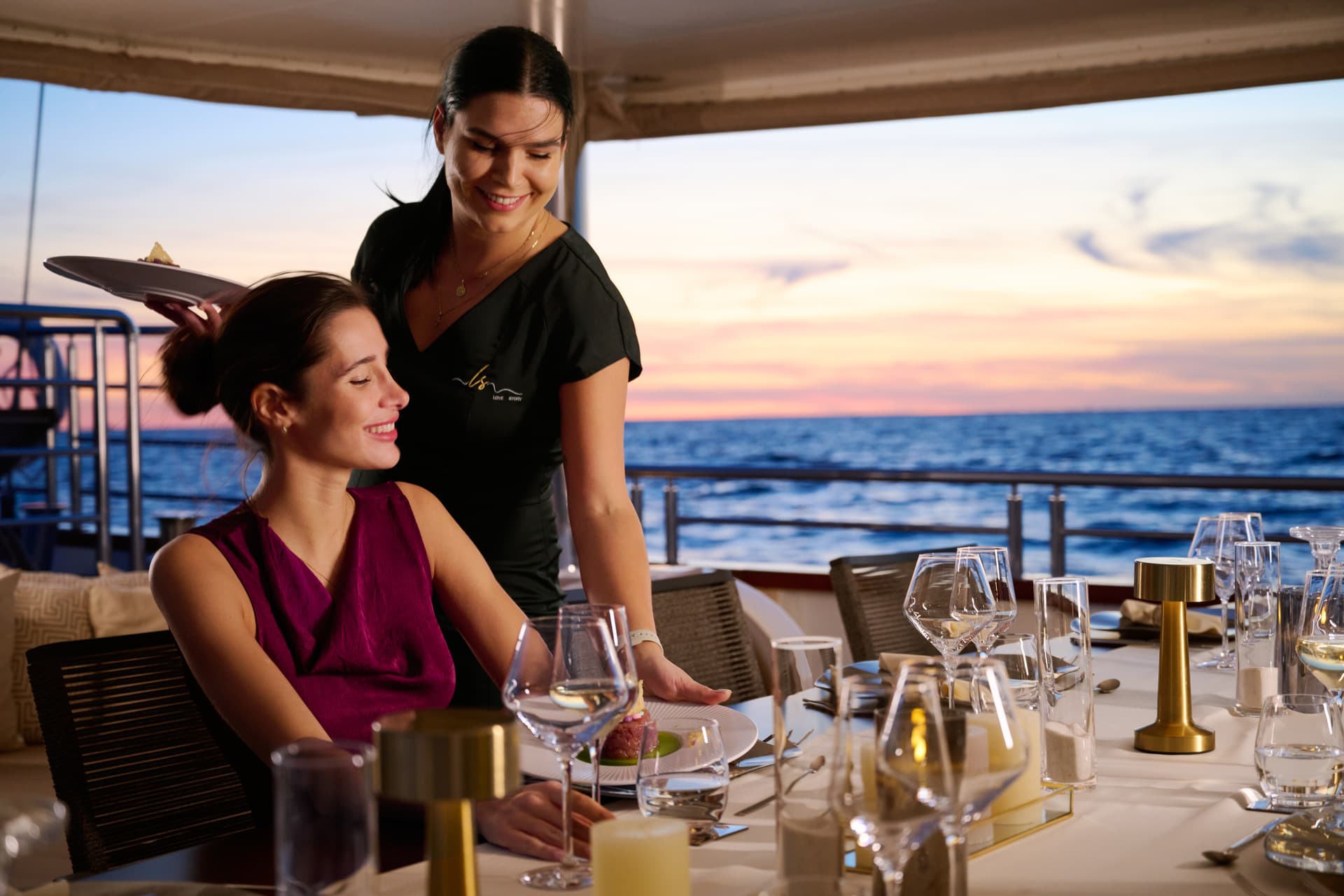 Fine dining service on a yacht deck at sunset over the ocean.