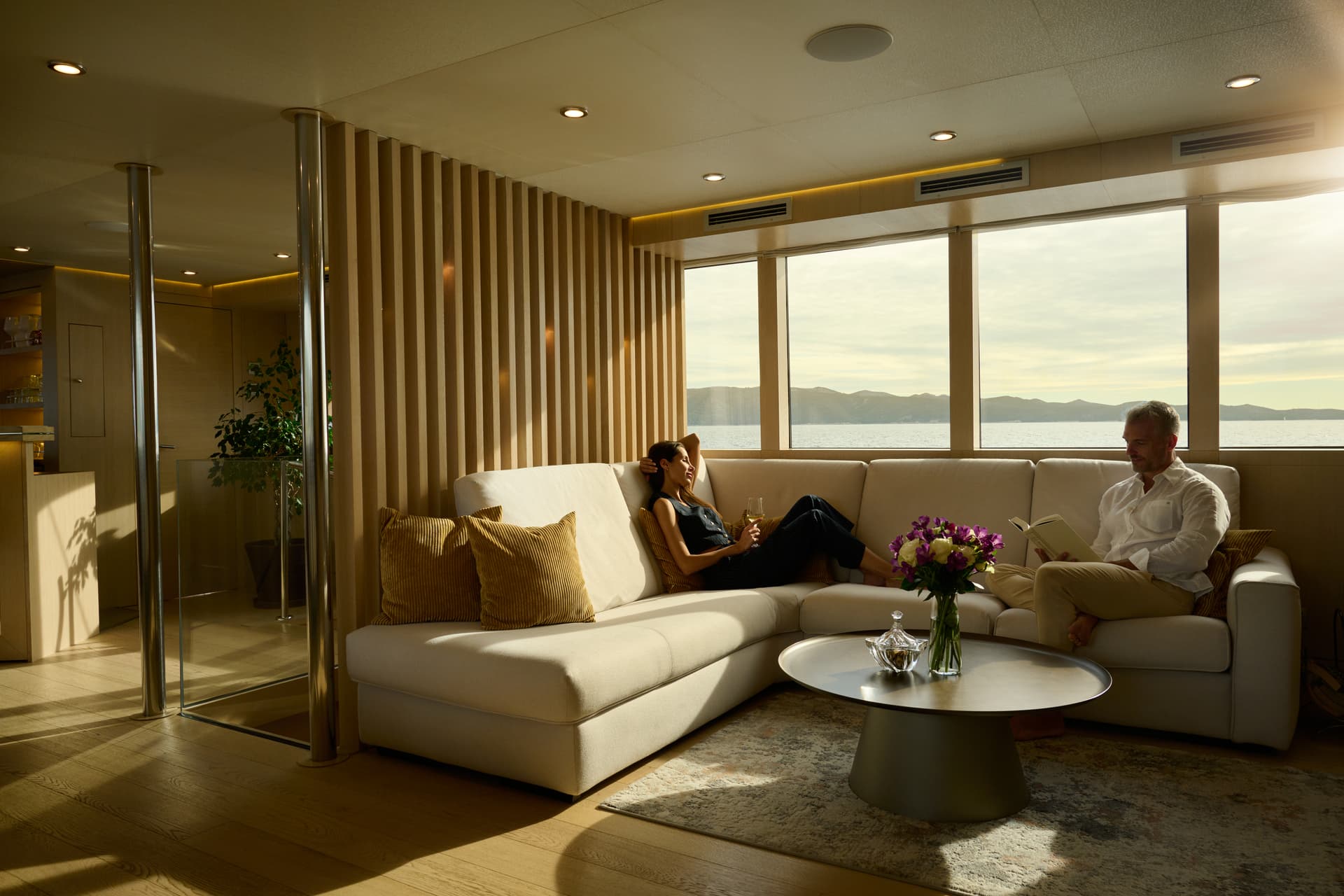 Couple relaxing in modern yacht salon with sea and mountain view outside windows