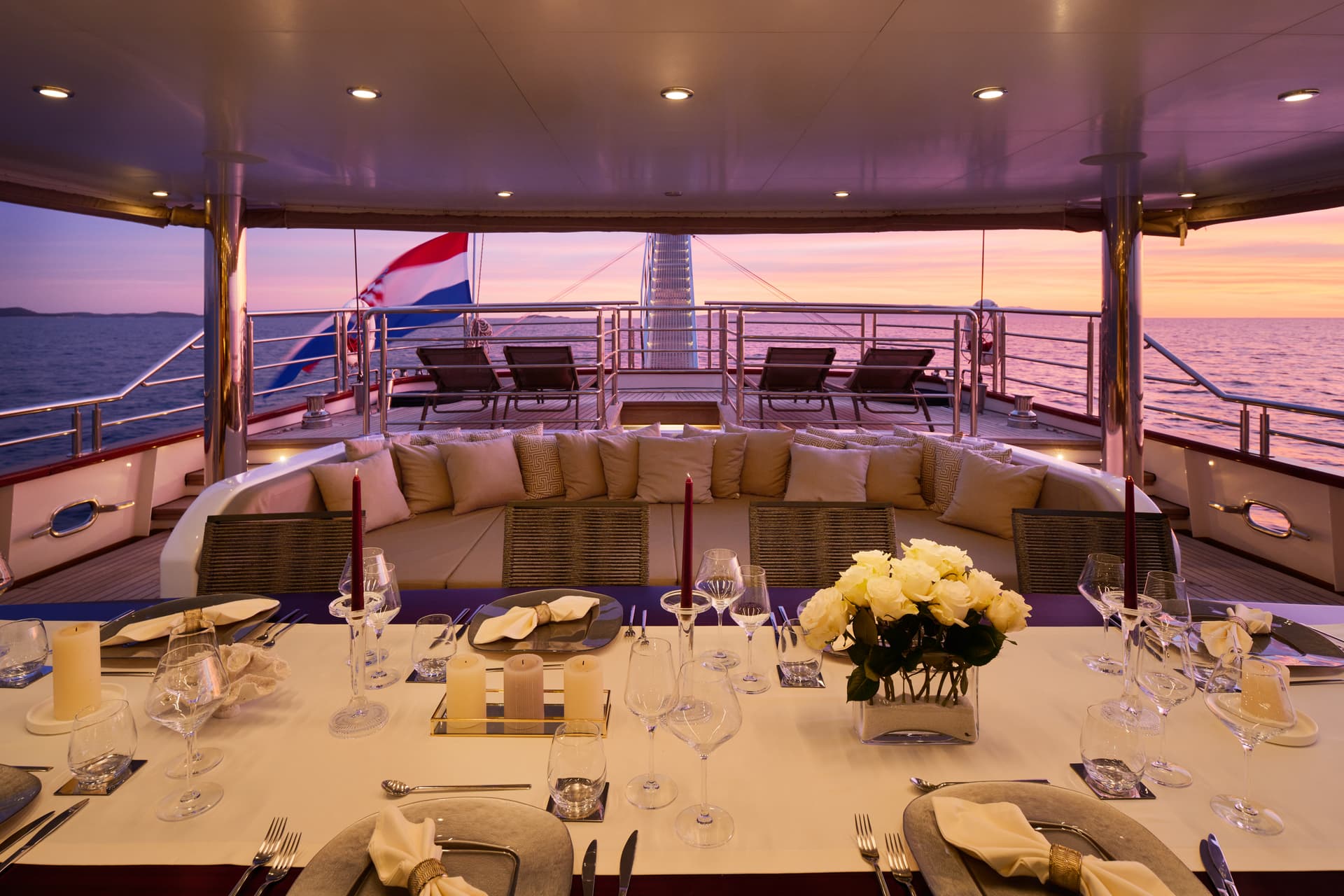 Yacht dining table set for sunset with Croatian flag flying over coastal waters