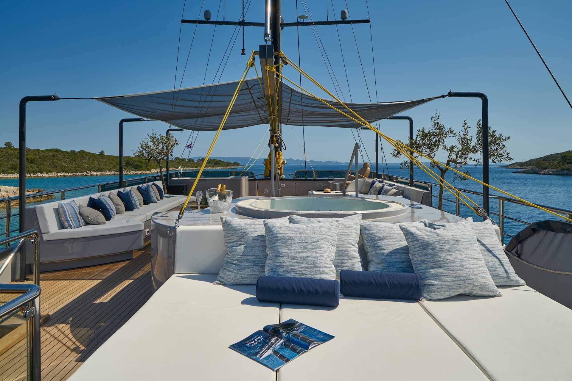 Luxury yacht deck with jacuzzi, sun pads, and champagne anchored near a lush green coastline.