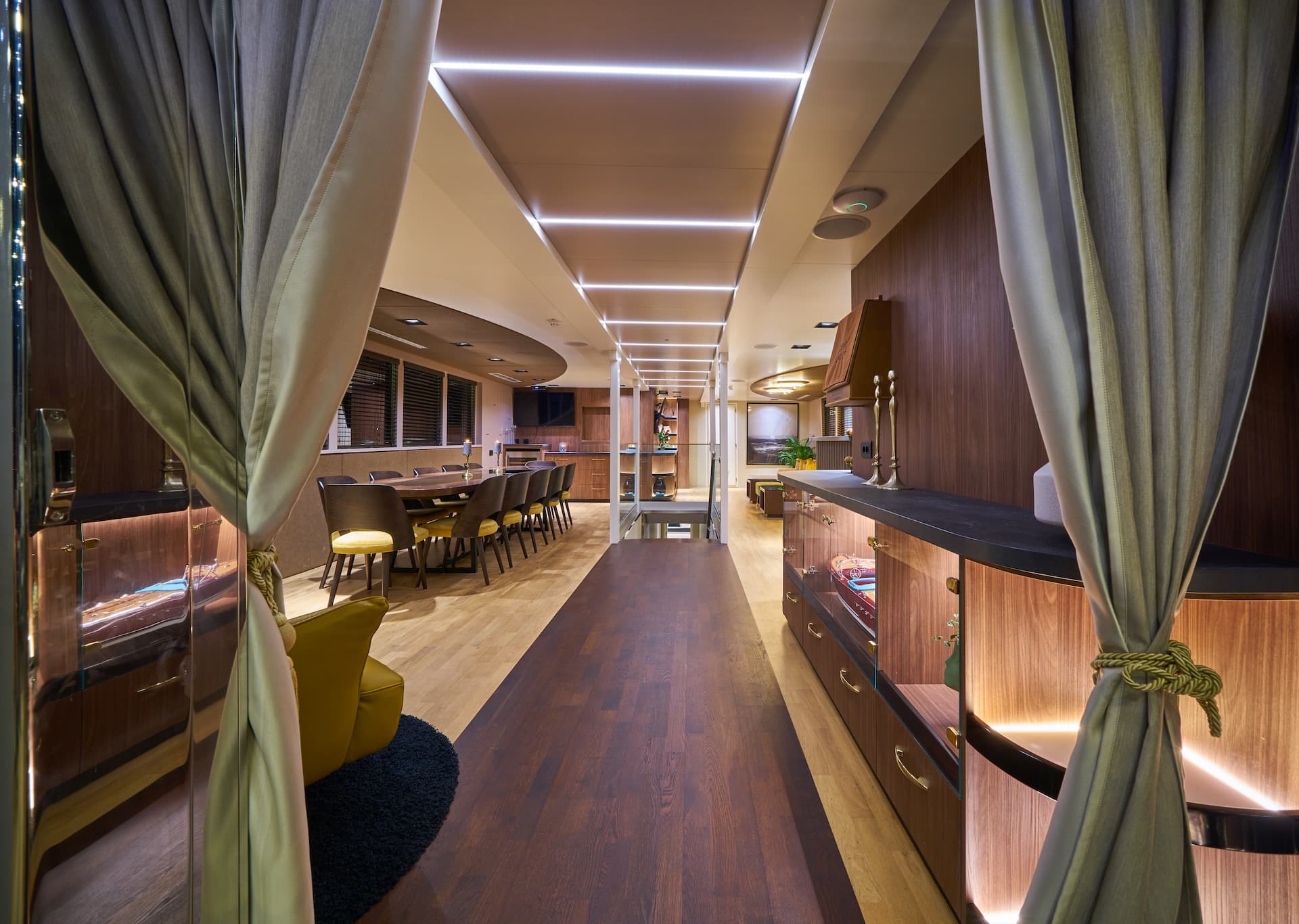 Luxury yacht interior hallway with wood paneling, recessed lighting, and dining area.