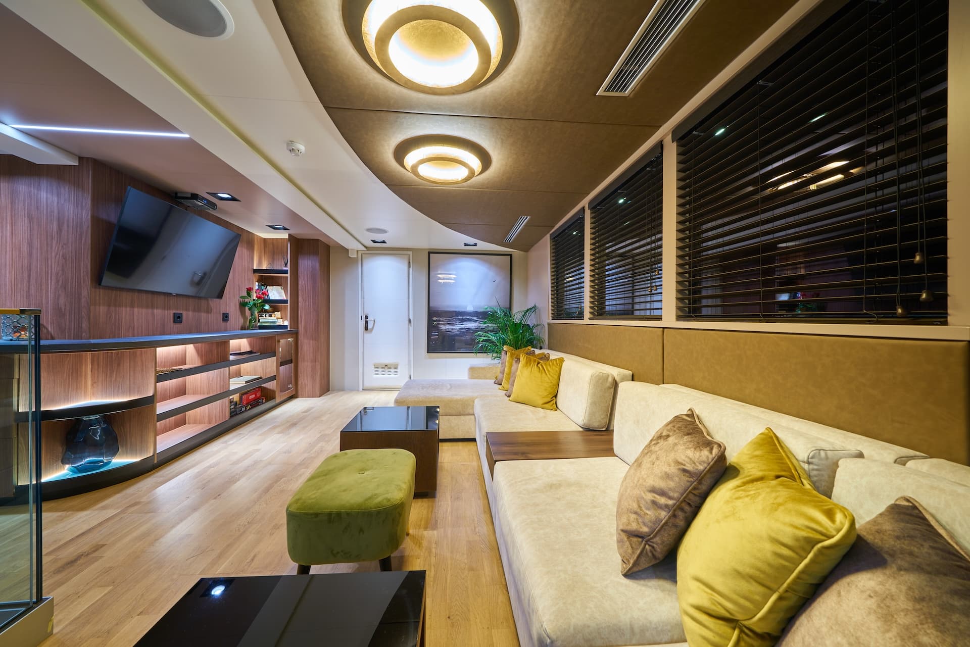 Luxurious yacht lounge interior with wood paneling, modern lighting, and beige sectional sofa.
