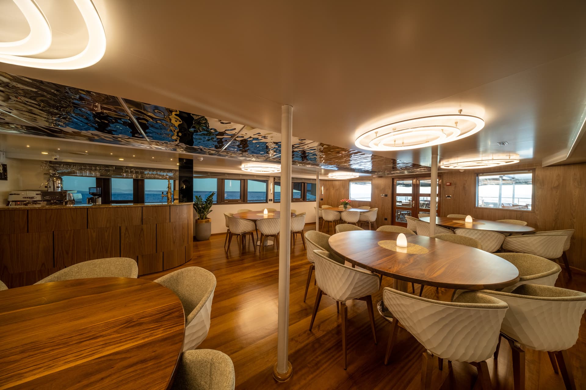 Dining room interior on a yacht with wood paneling, modern chairs, and views of the sea.