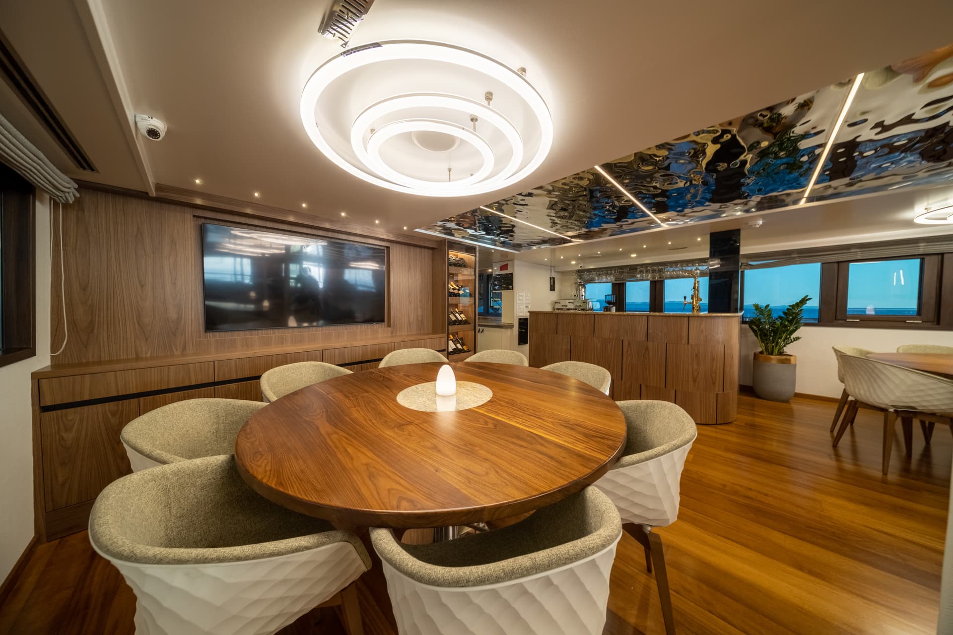 Modern yacht dining area with wood paneling, round table, and view of the sea.