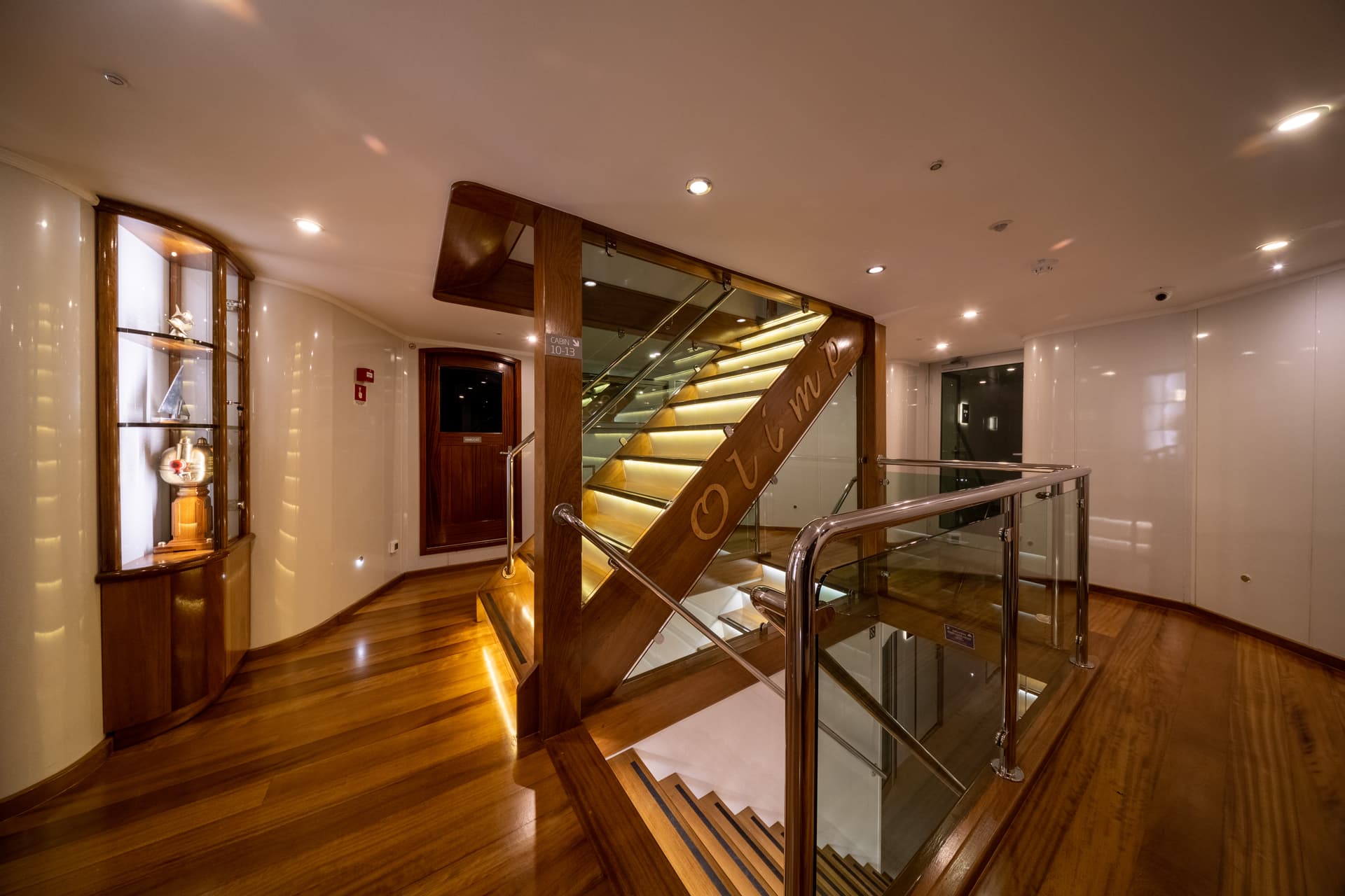Interior staircase with illuminated wood steps and "Olimp" carved on the banister inside a yacht.