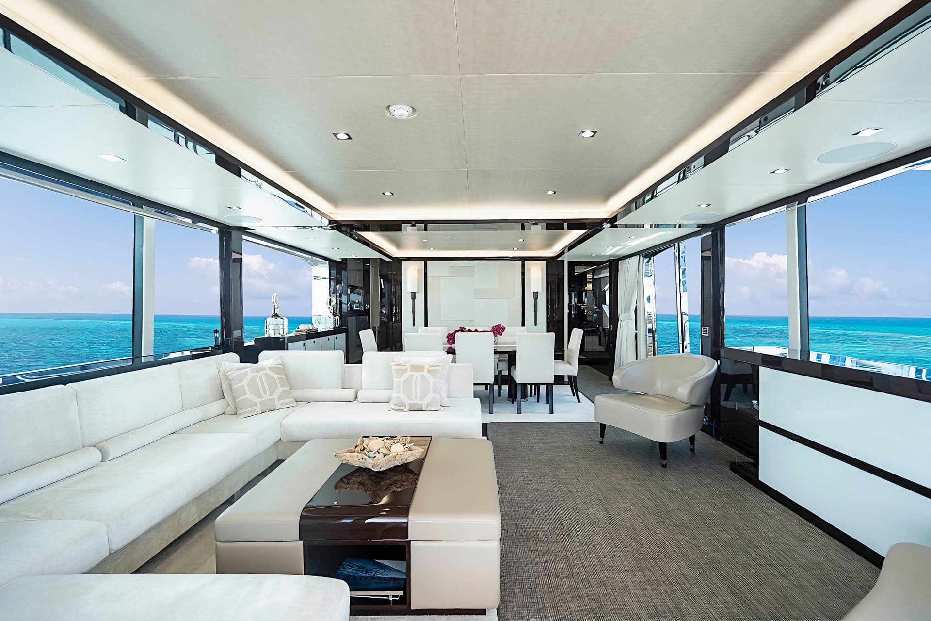 Luxury yacht interior with white seating and dining area overlooking turquoise ocean water.