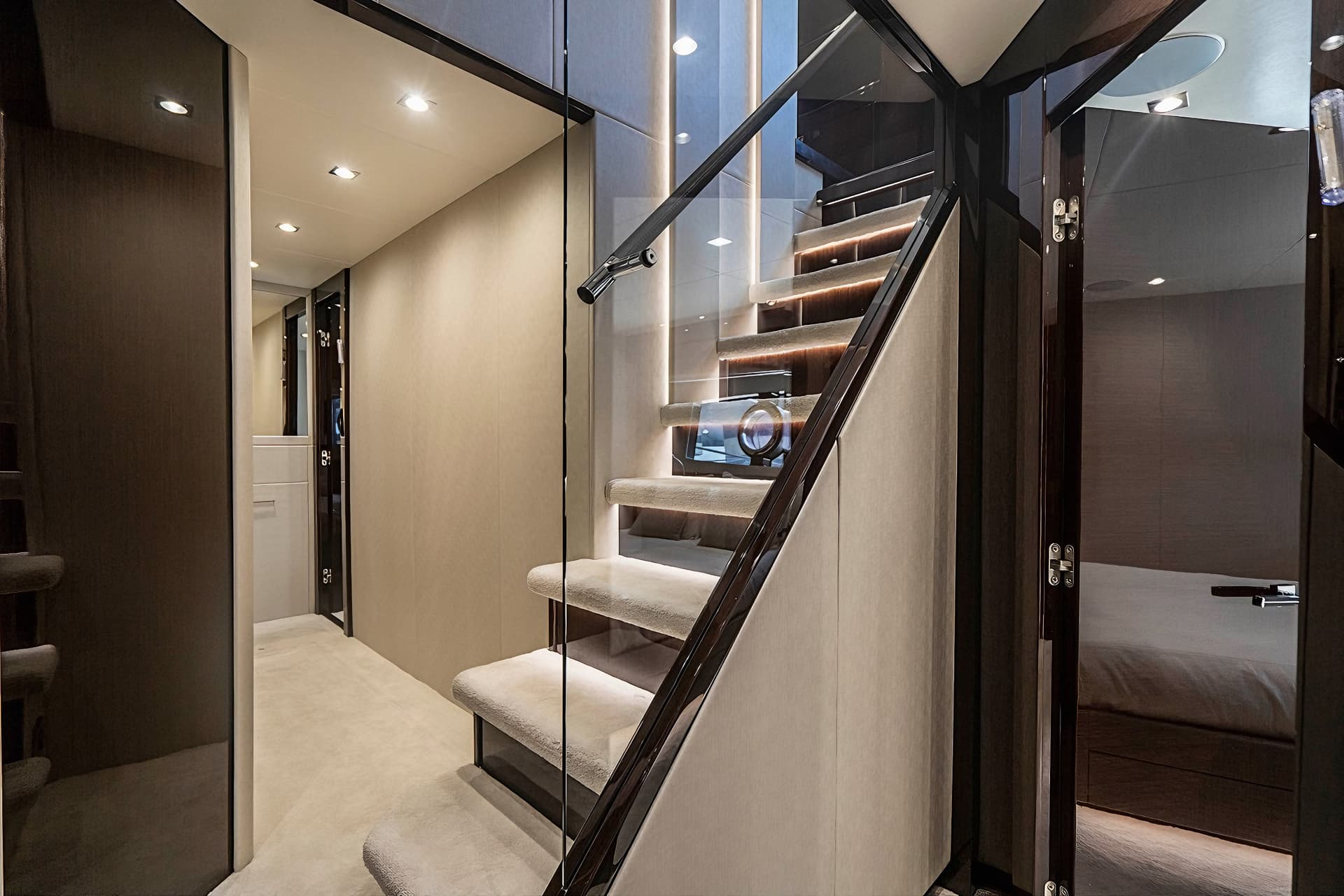 Luxurious interior staircase with carpeted steps and glass railing inside a yacht.