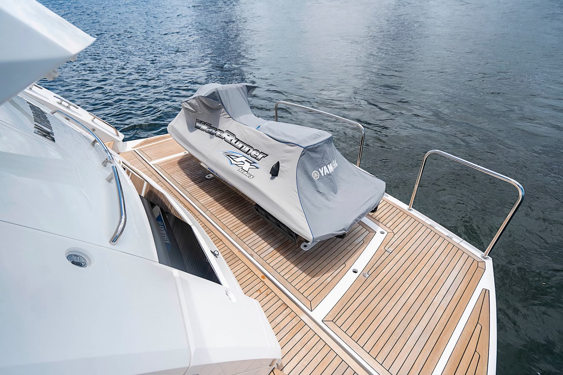 Covered Yamaha WaveRunner on teak swim platform of a white yacht on dark water.