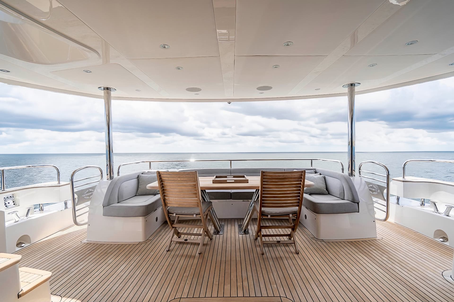 Teak deck seating area on a yacht looking out over the ocean under a cloudy sky.