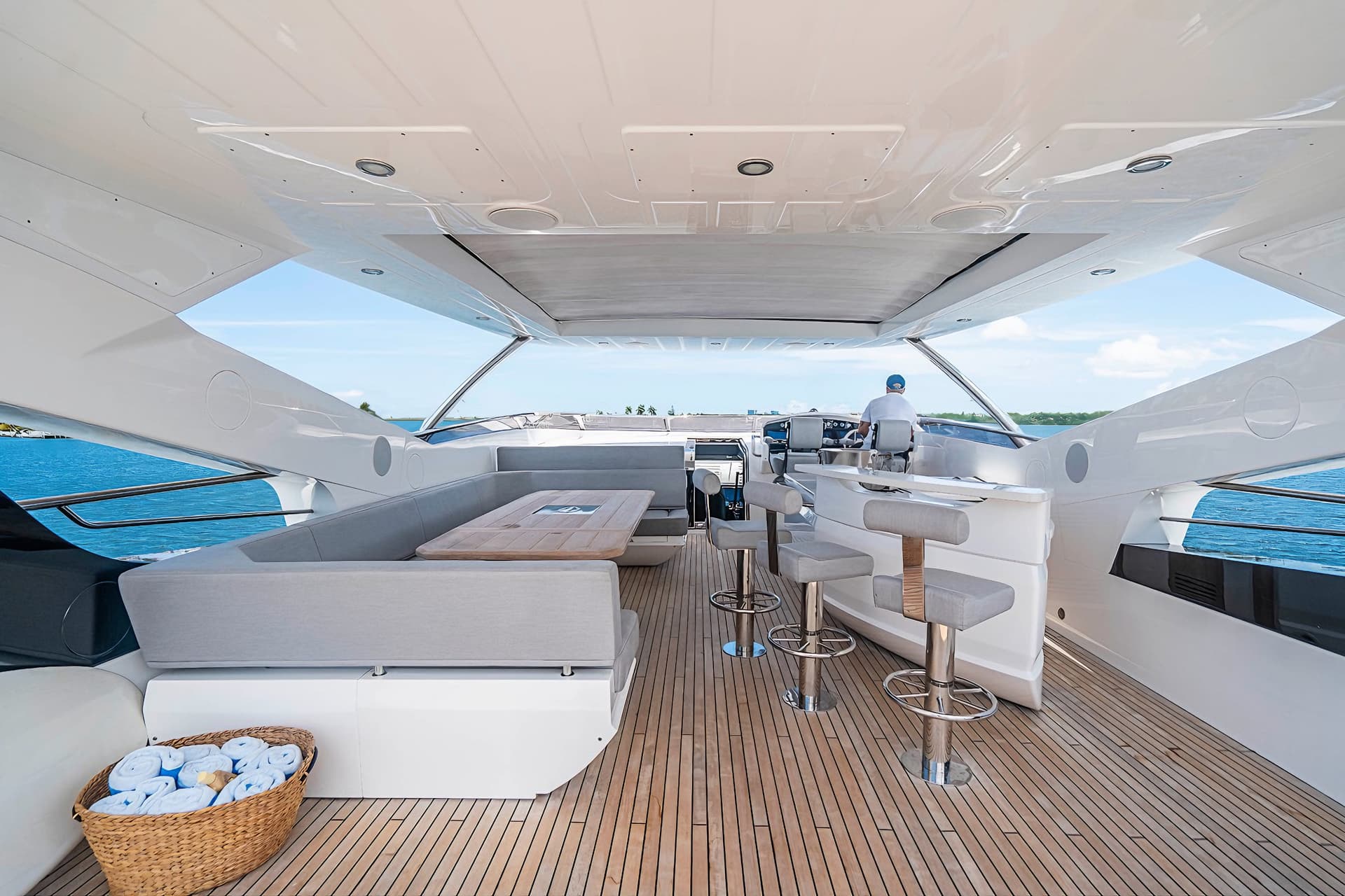 Aft deck of a luxury yacht with teak flooring, seating area, helm station, and blue water visible.