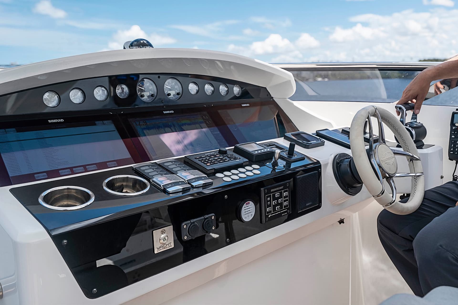 Yacht helm station with digital displays, controls, and white steering wheel under blue sky.
