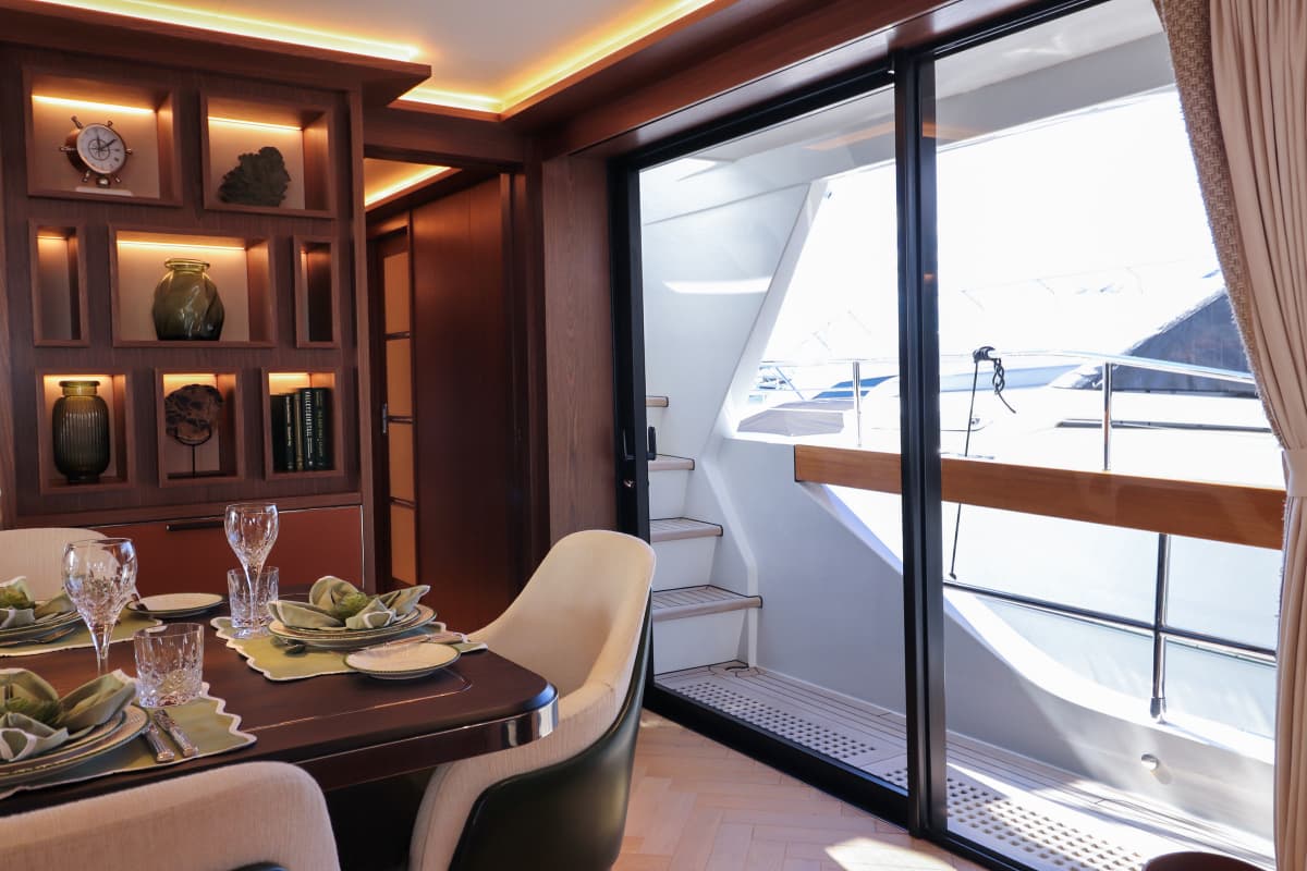 Yacht interior dining area with wood paneling, set table, and view of exterior deck.