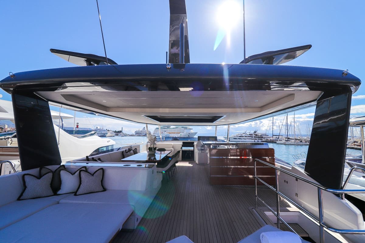 Flybridge deck of a luxury yacht showing seating area overlooking a busy harbor with cruise ships.