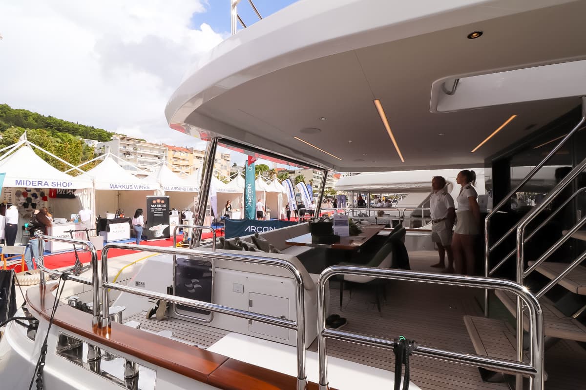 View from yacht deck toward outdoor exhibition tents and hillside buildings.