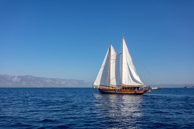 Wooden gulet sailboat with white sails on deep blue sea near Croatian coastline mountains.