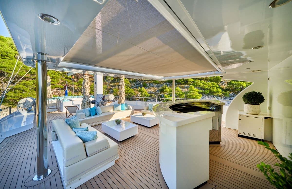 Luxury yacht deck with white seating, bar, and lush green coastline view.