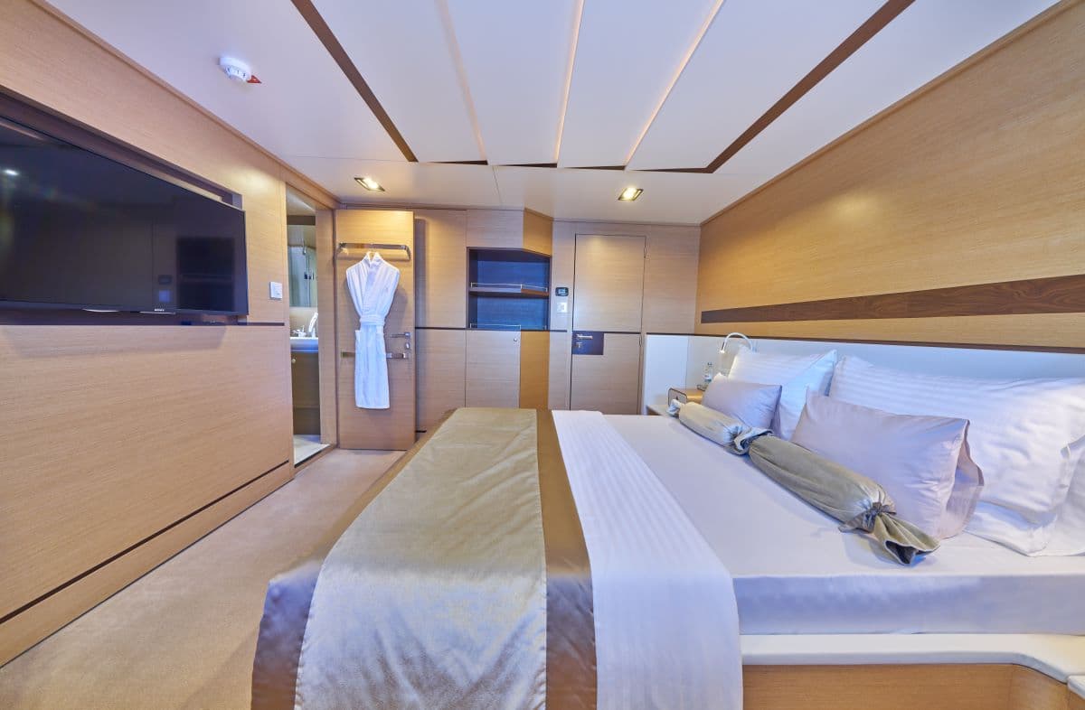 Modern yacht cabin bedroom with wood paneling, large bed, and wall-mounted television.