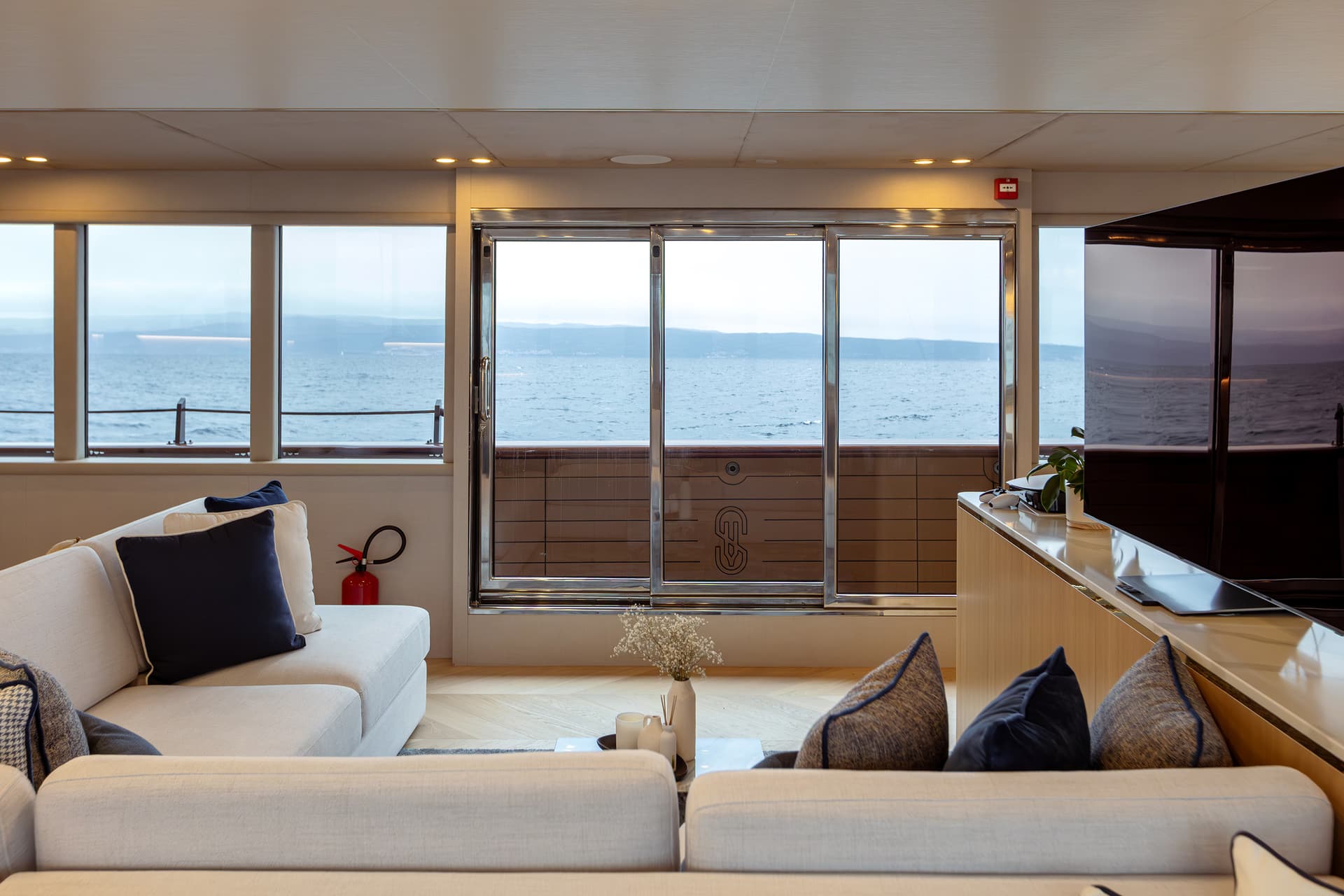 Luxury yacht interior lounge with light sofa and view of the sea and distant coastline.