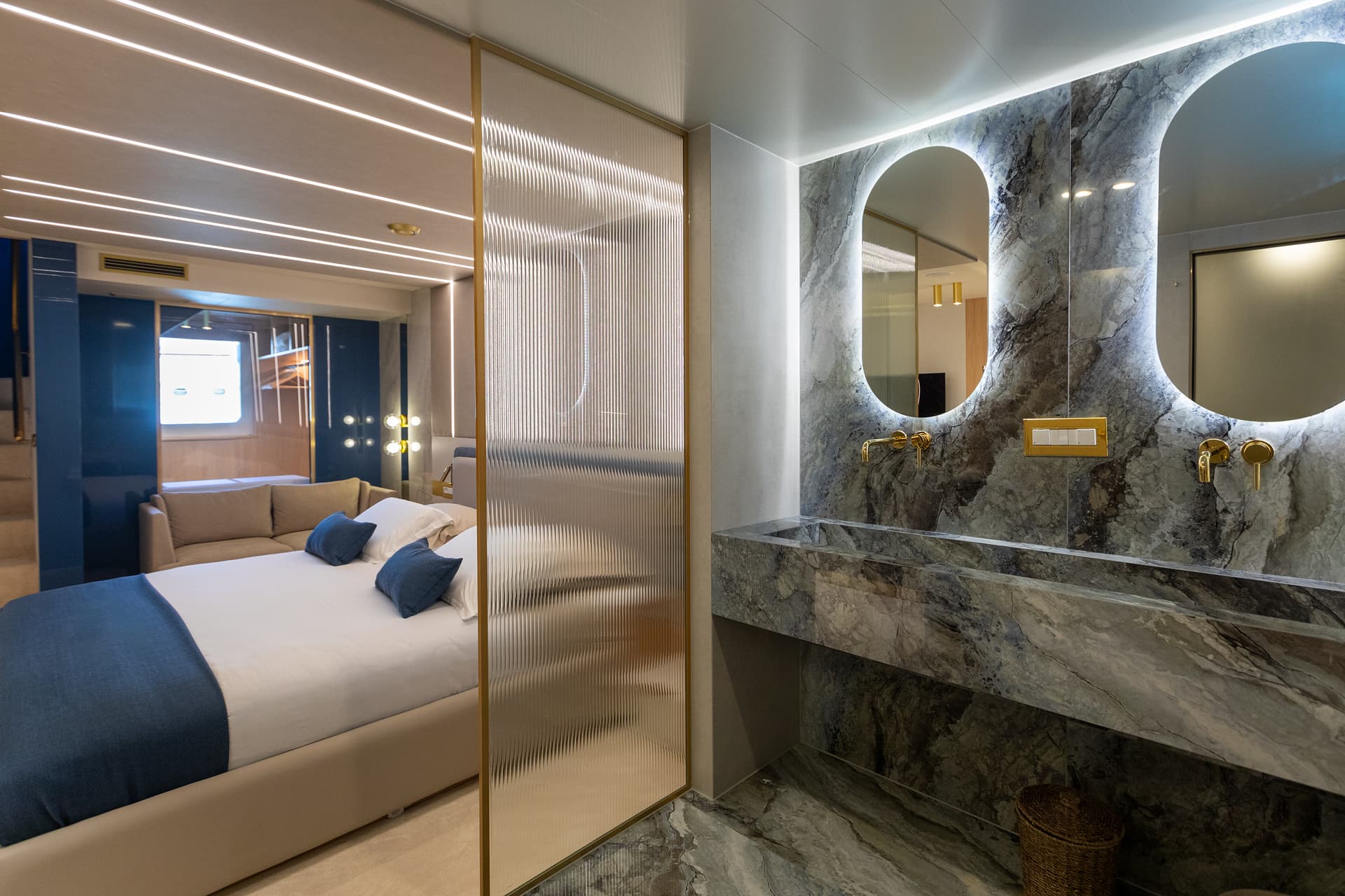 Modern yacht master cabin with marble vanity, backlit mirrors, and view of sleeping area.