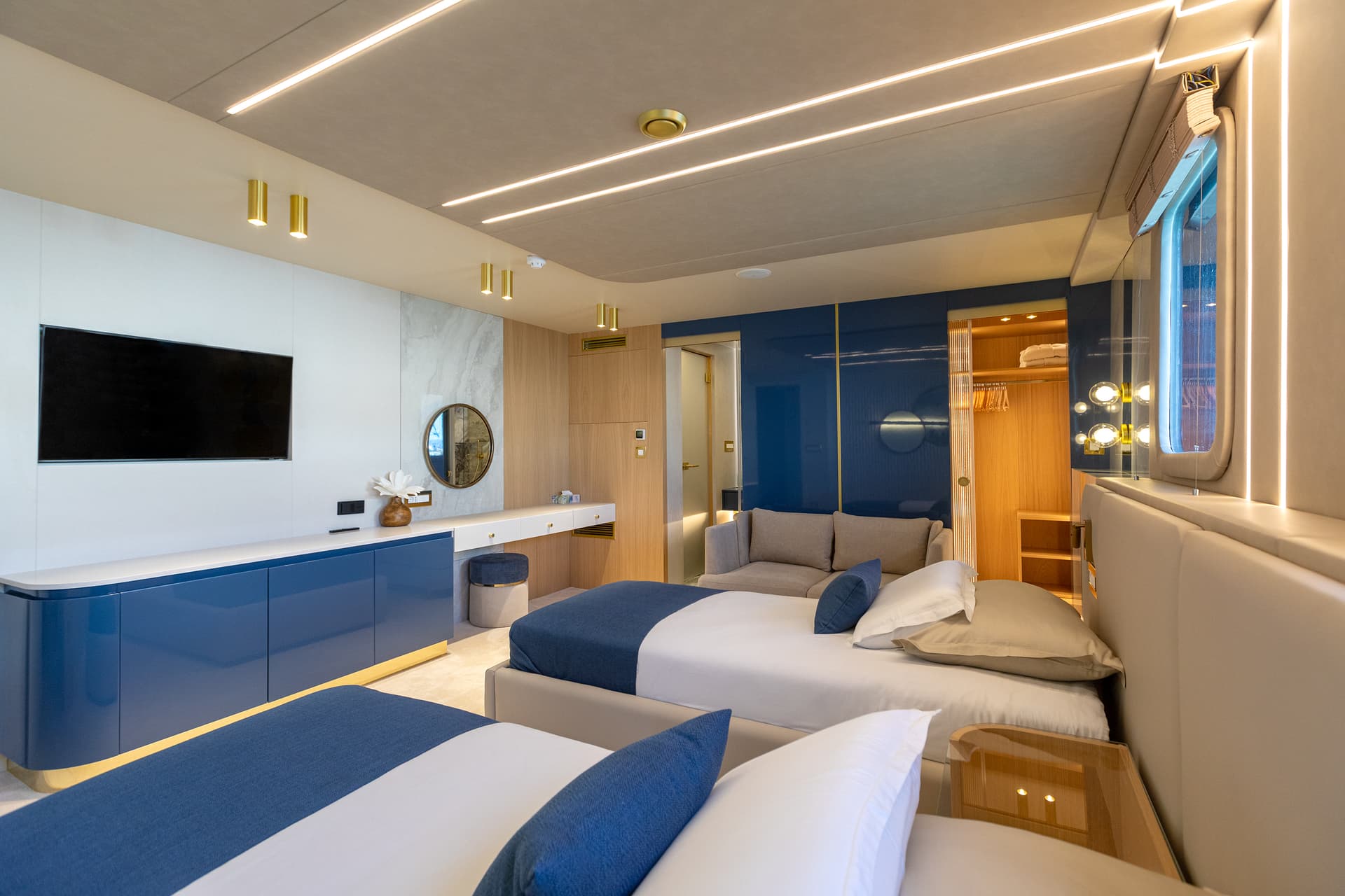 Modern yacht cabin interior with twin beds, blue accents, wood paneling, and integrated lighting.