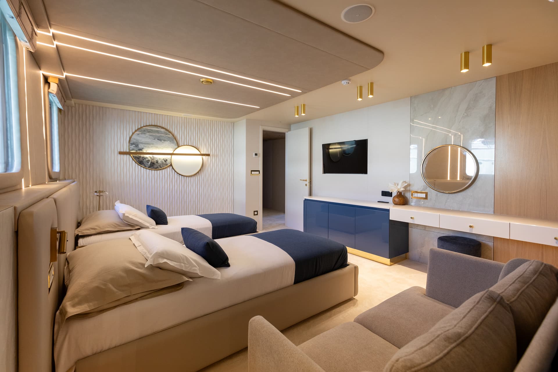 Twin beds and seating area inside a modern, well-lit yacht cabin.