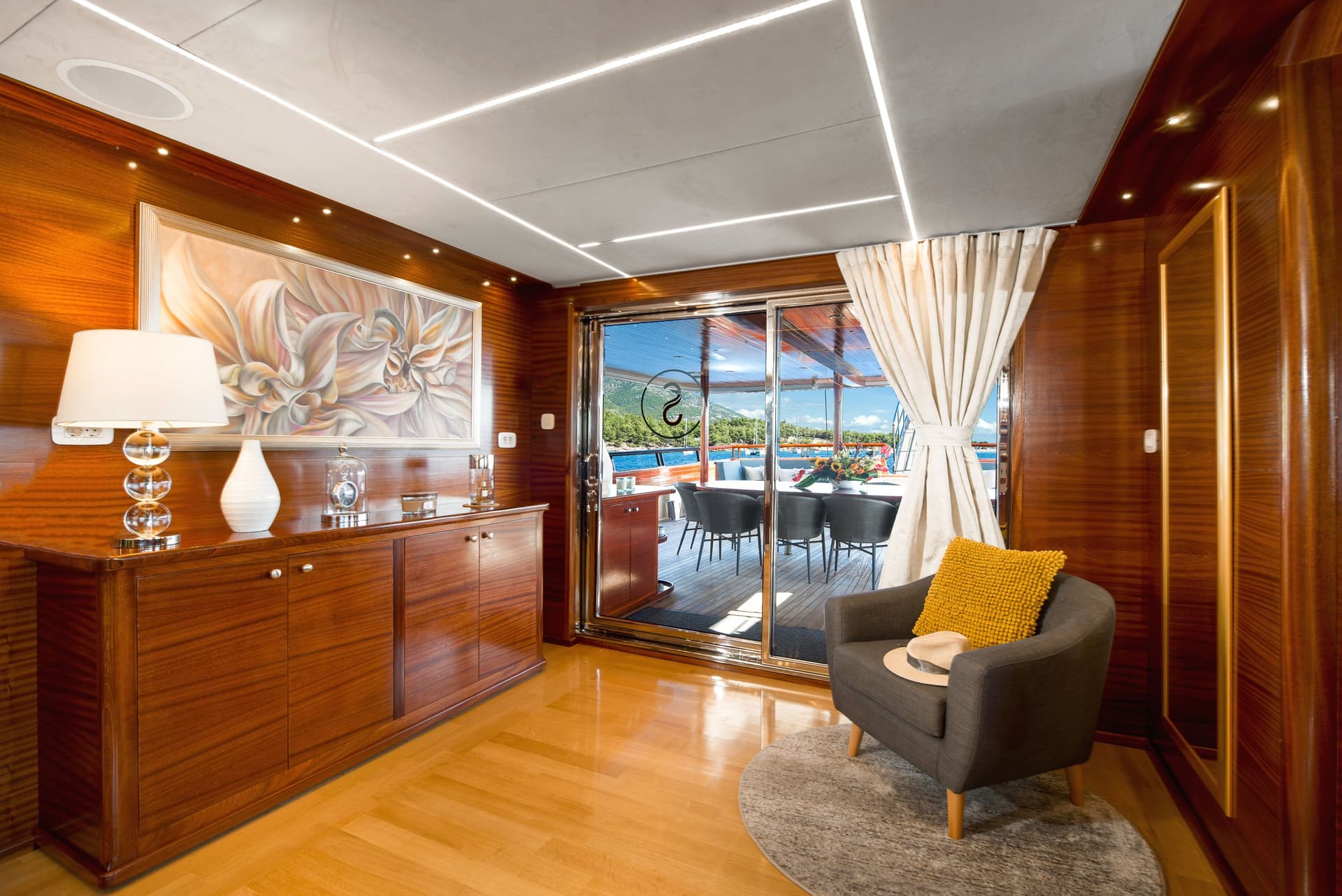 Luxury yacht interior with wood paneling opening to deck overlooking sunny coastal waters