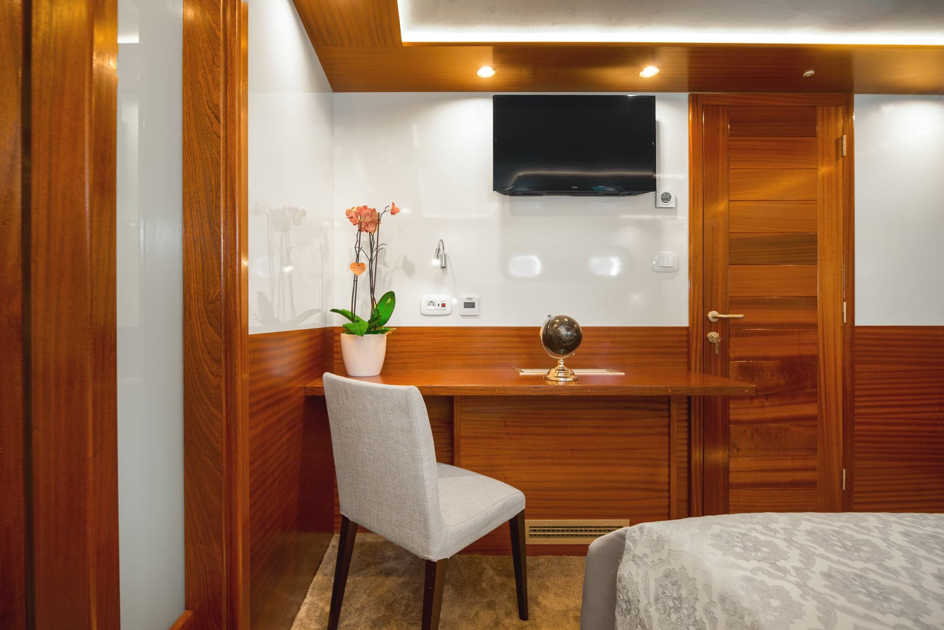 Desk area in a cabin with wood paneling, a chair, an orchid, and a small globe.